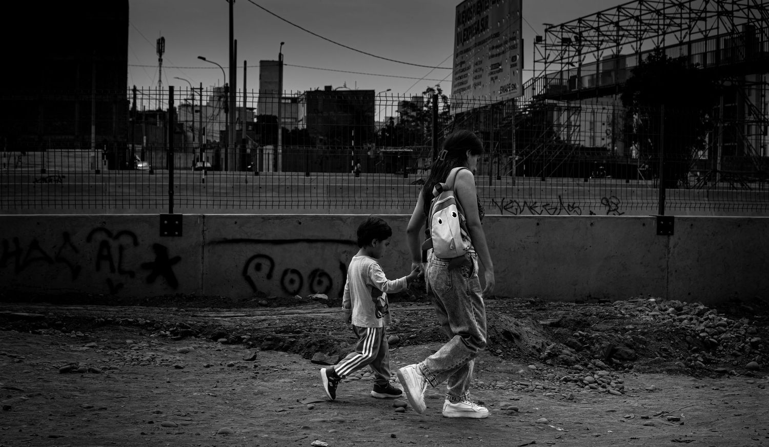 Two children walk hand in hand through urban landscape in black and white photo.