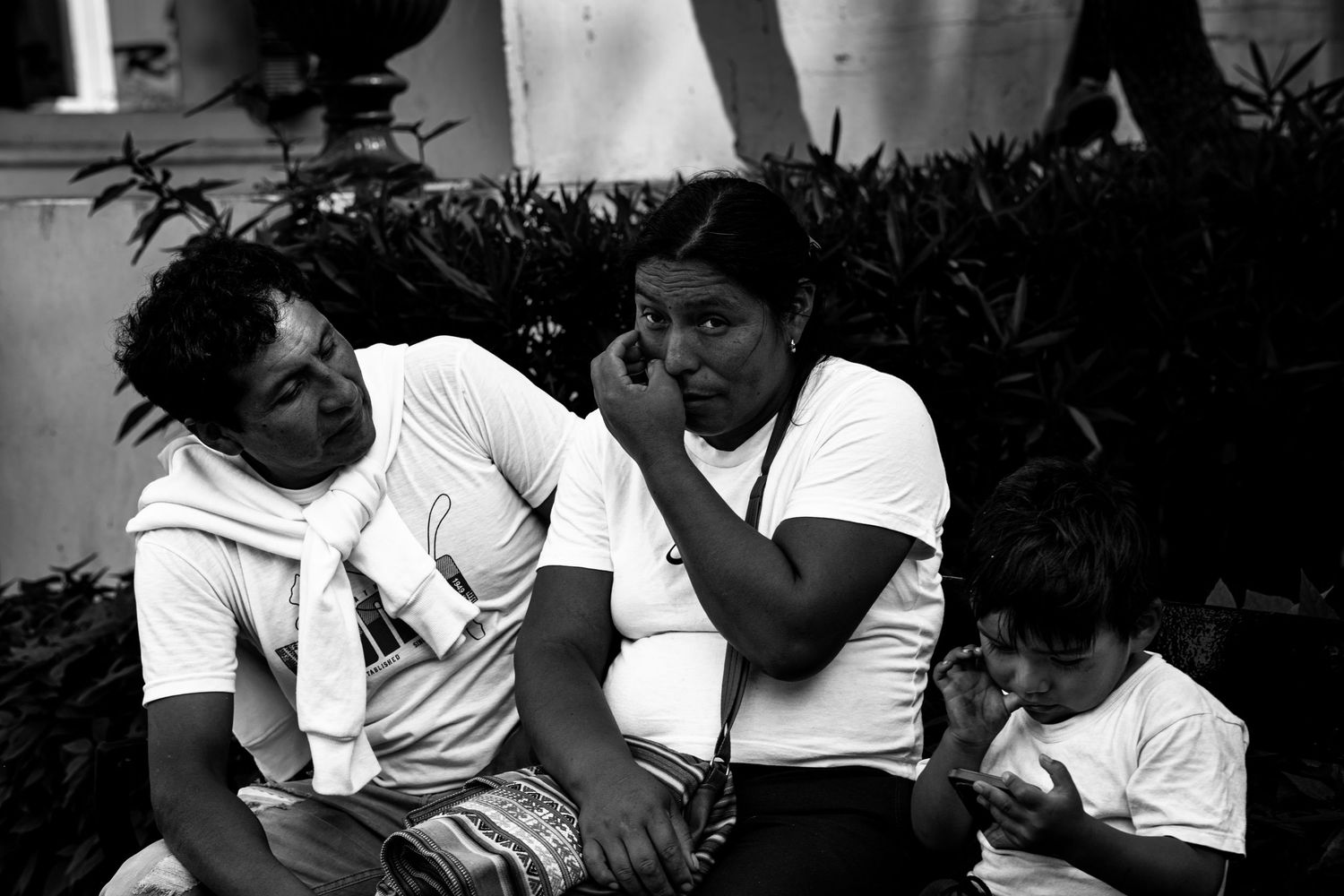Three people sit outdoors together in candid black and white street photography.