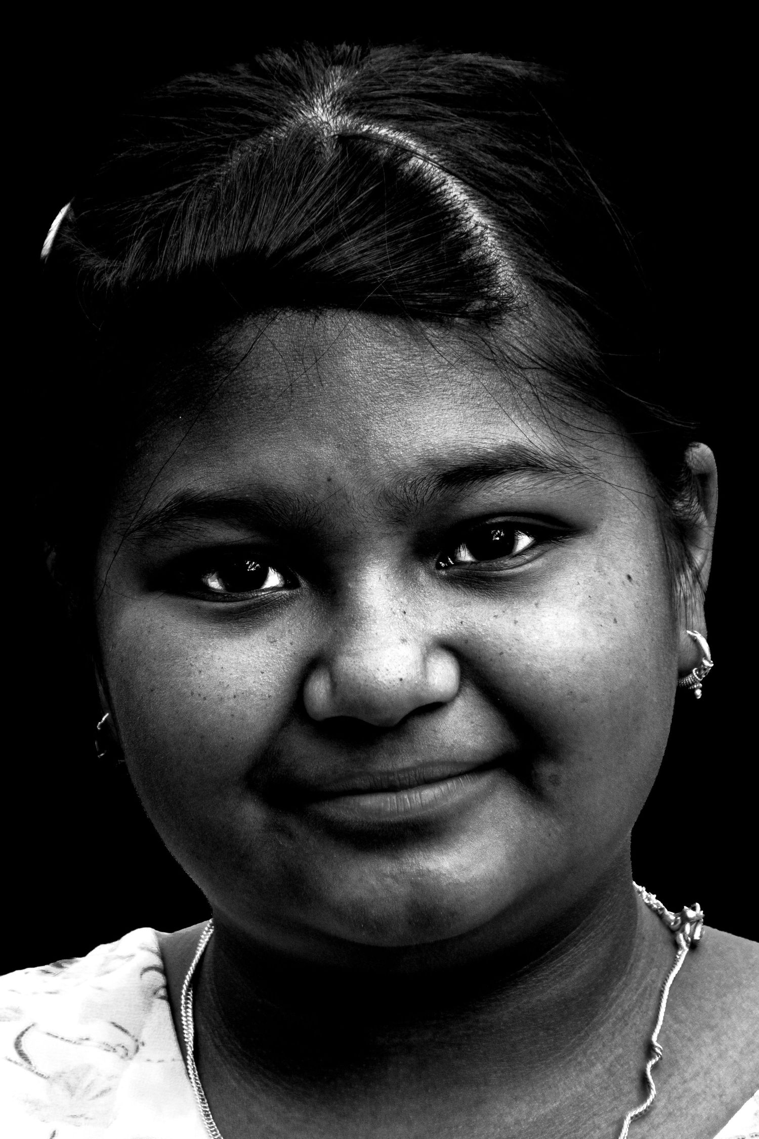 Black and white portrait of a young Indian girl smiling softly against a dark background.