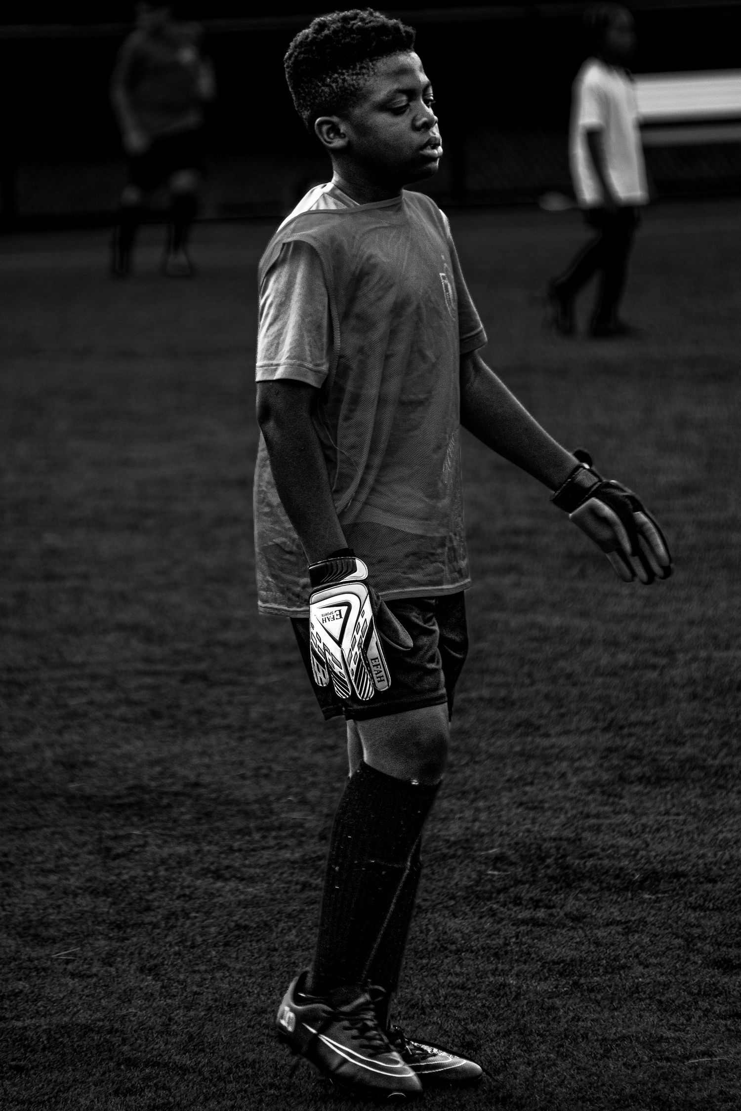 Young goalkeeper wearing gloves standing on soccer field in black and white portrait.