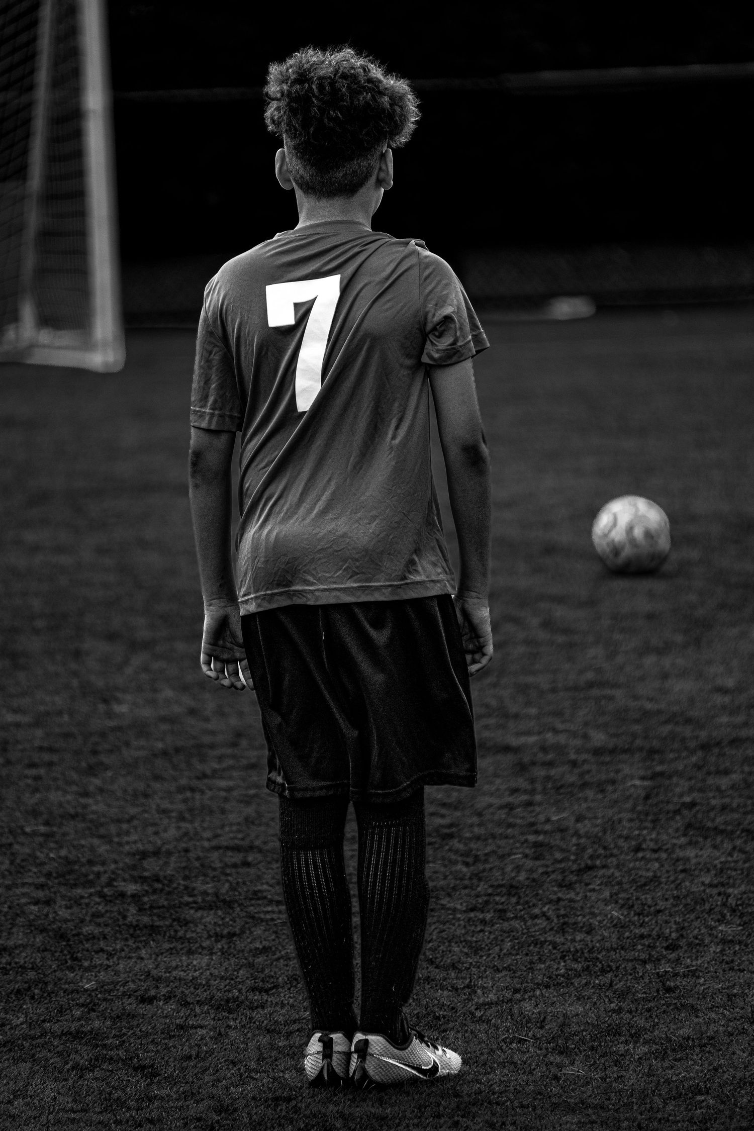 Rear view of youth soccer player wearing number 7 jersey facing goal in black and white.