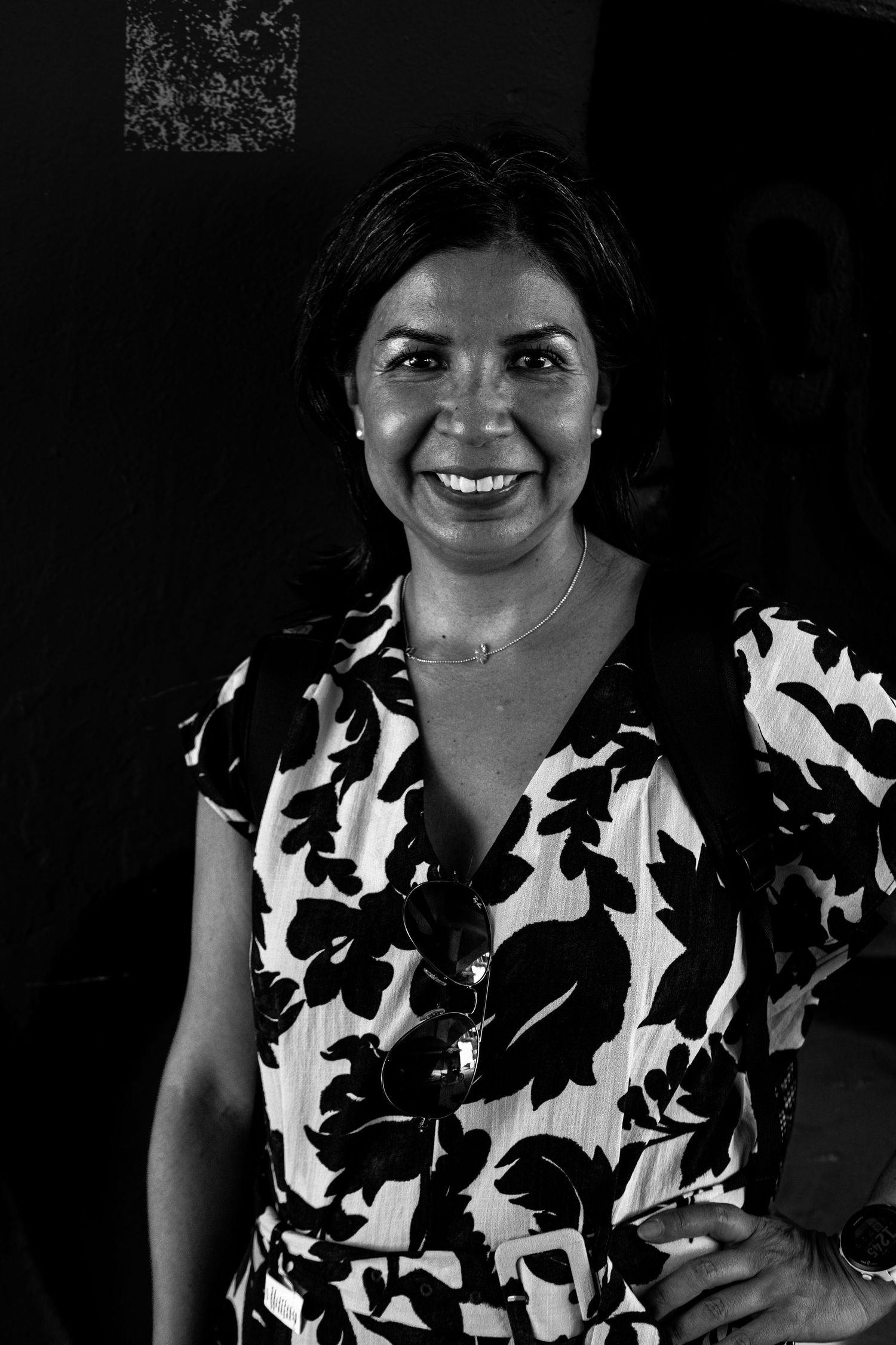 Black and white portrait of a smiling woman in a floral dress wearing a necklace indoors.