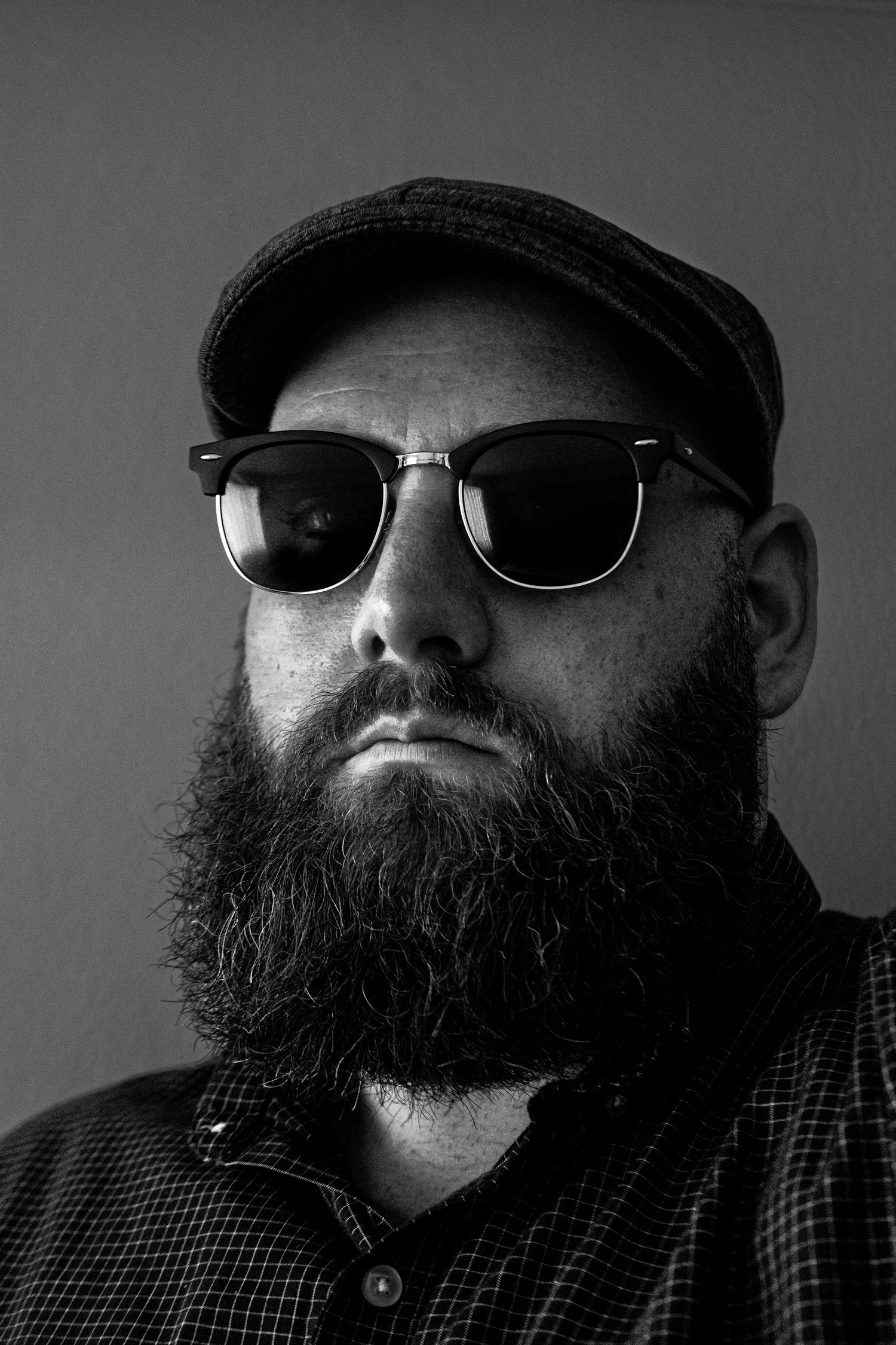 Black and white portrait of a bearded man wearing sunglasses and a flat cap.