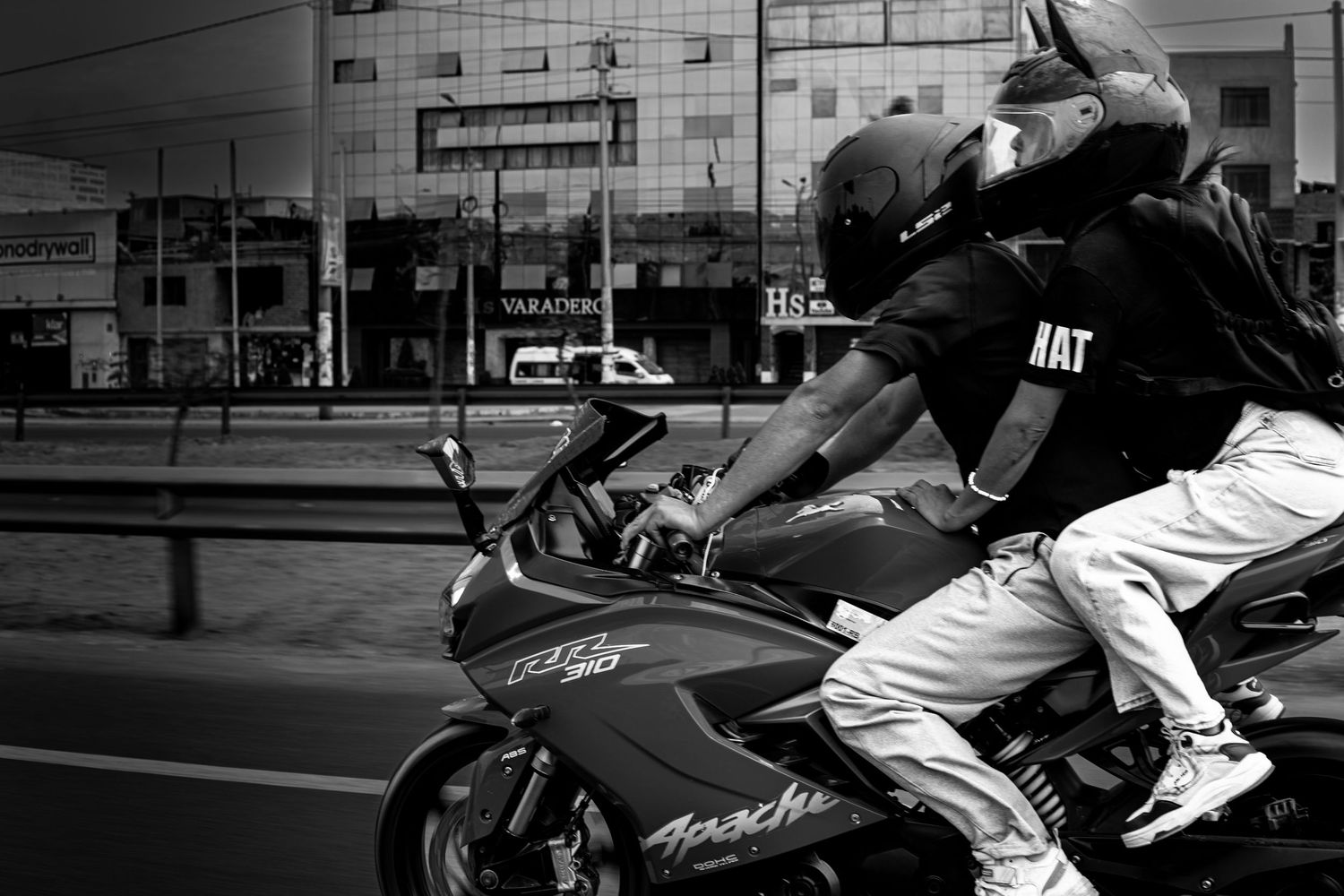 Black and white photo of two people riding a sport motorcycle through a busy city street.