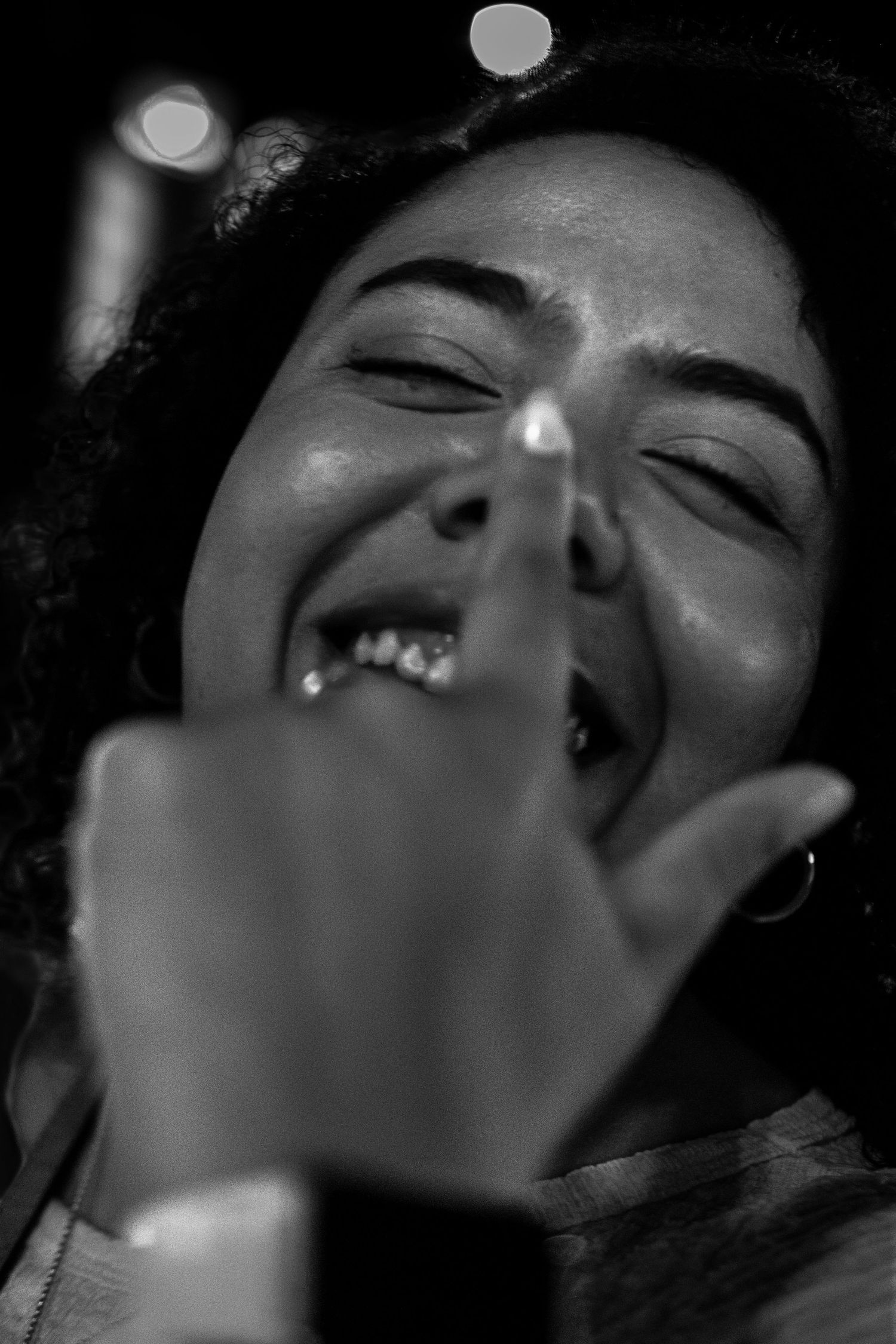 Black and white close-up of a laughing woman with curly hair pointing finger at camera.