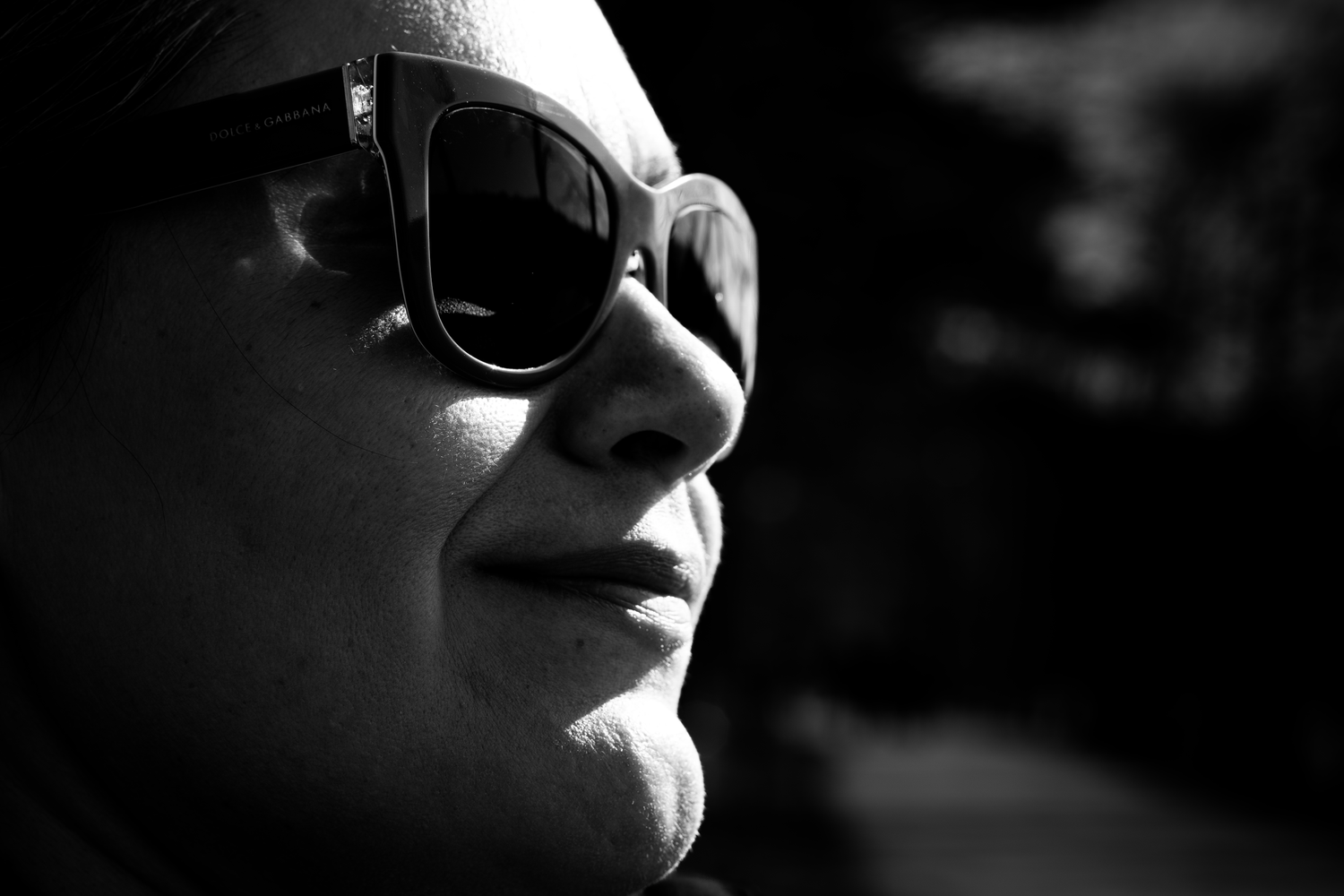 Black and white close-up profile of a woman wearing large sunglasses in bright sunlight.