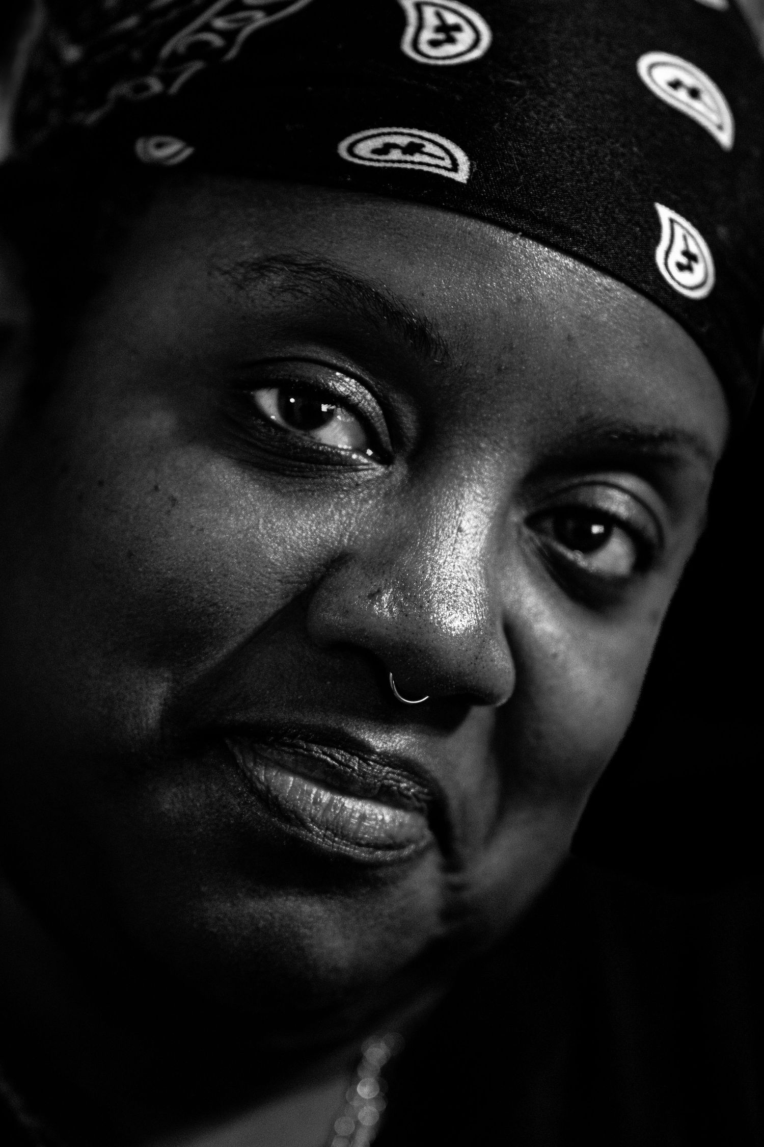 Black and white portrait of a woman wearing a bandana headscarf with a nose ring smiling.