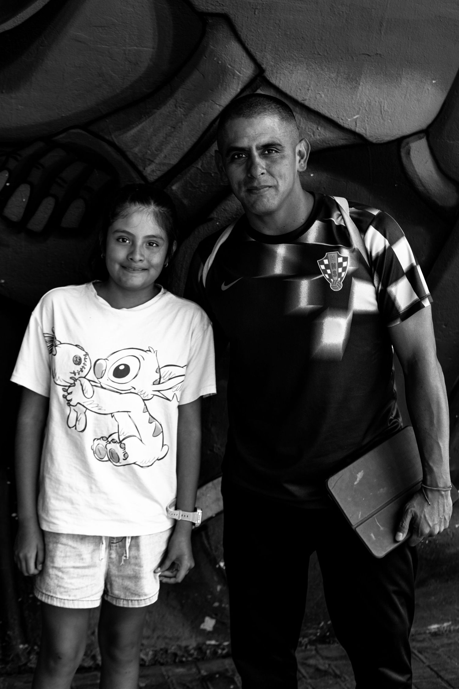 Man and young girl pose together in front of graffiti wall in black and white.