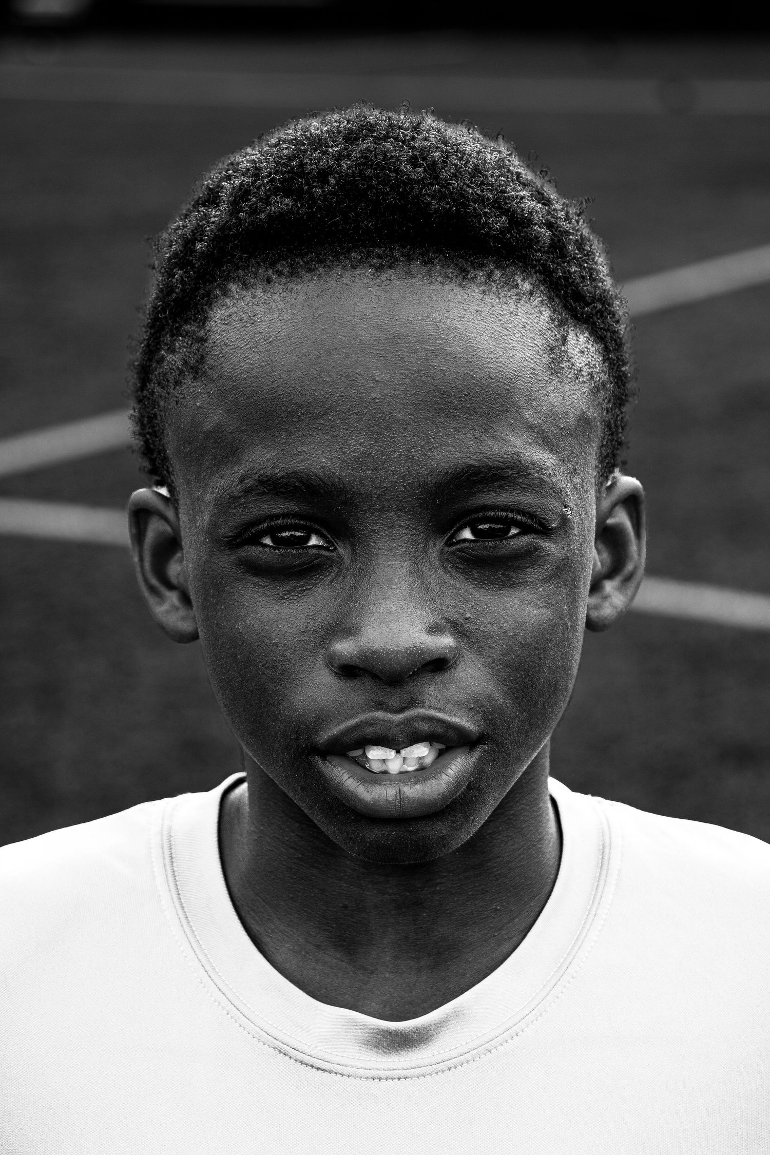 Close-up black and white portrait of young boy soccer player looking at camera on field.