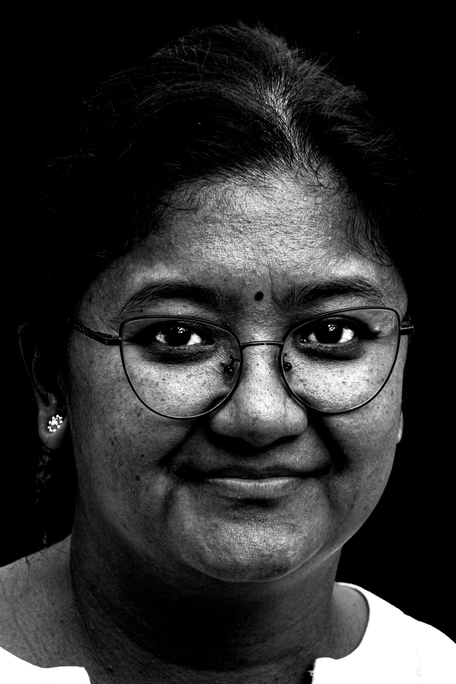 Black and white portrait of a smiling woman wearing round glasses with a bindi on her forehead.