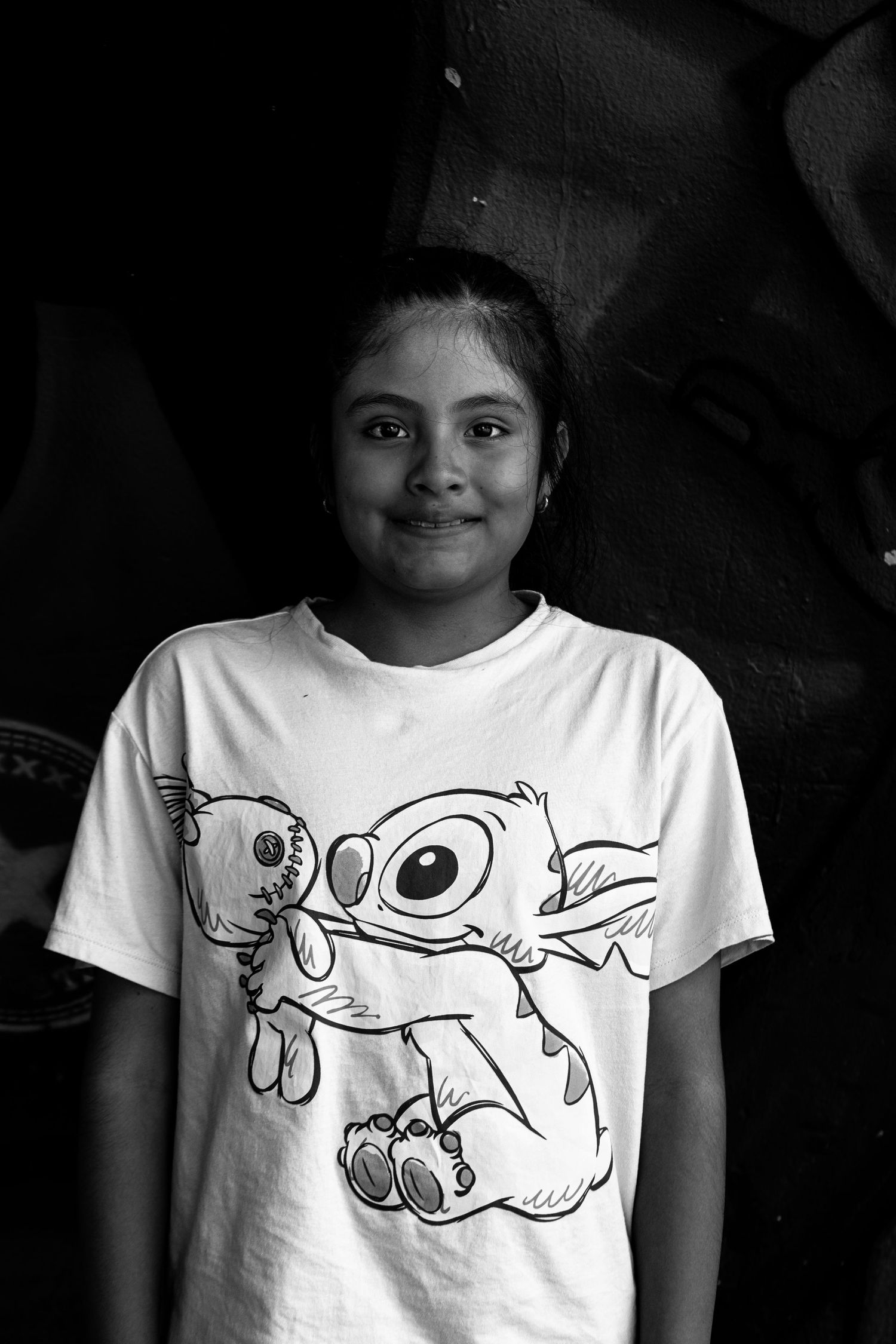 Black and white portrait of a young girl smiling while wearing a Lilo and Stitch graphic t-shirt.