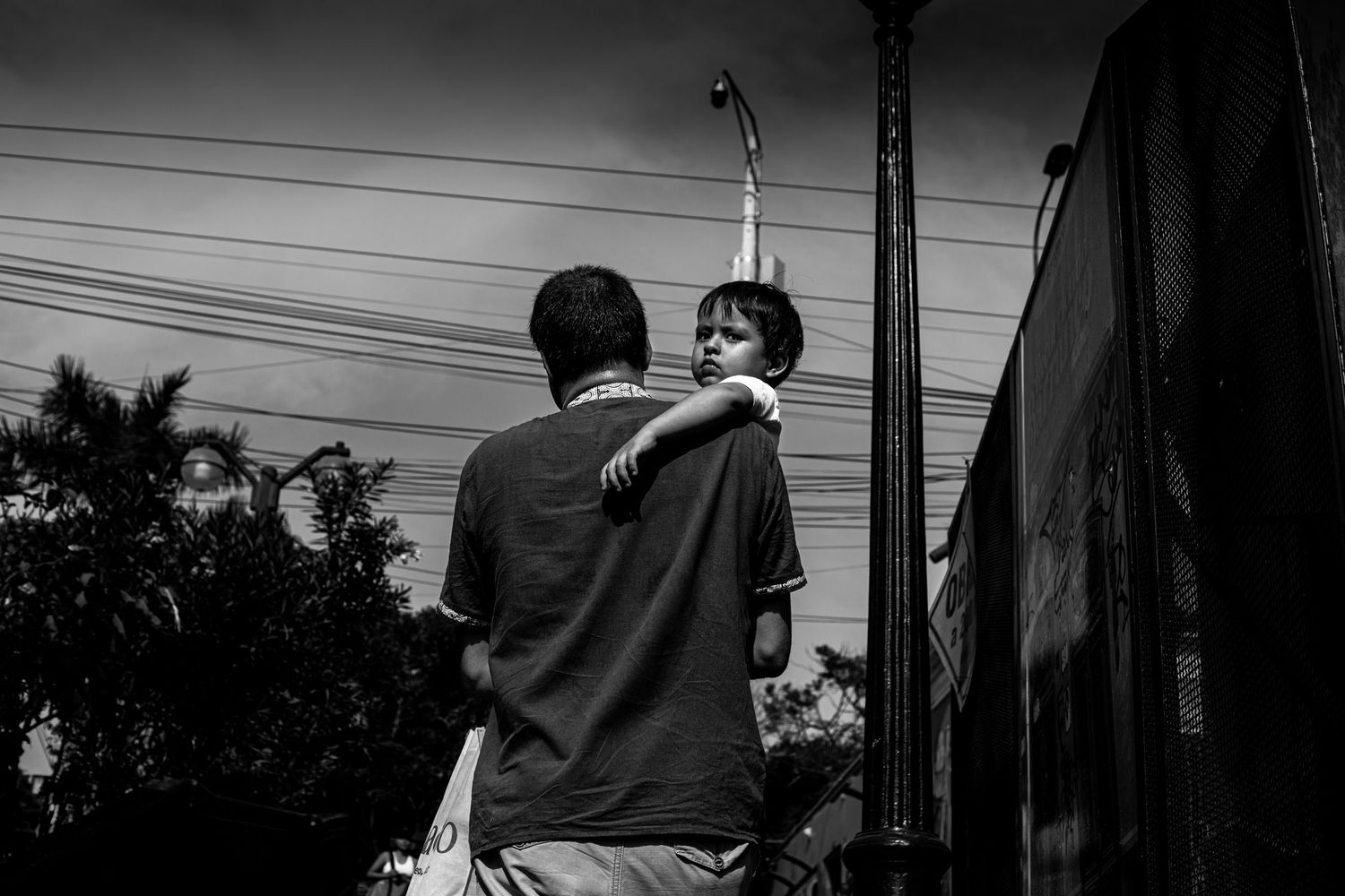 Father holds young child on shoulders in black and white outdoor photography.