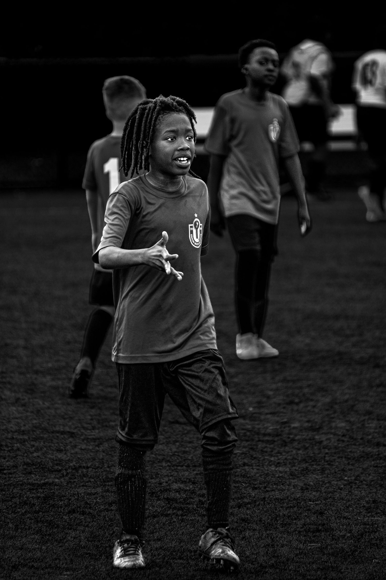 Energetic young soccer player with dreadlocks smiling on field in black and white photo.