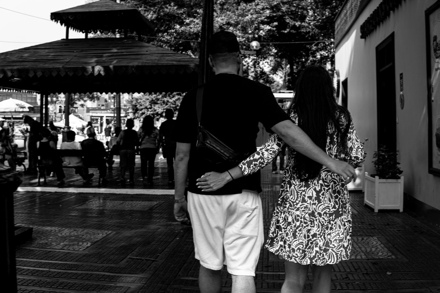 Black and white photo of a couple embracing while walking through a sunny outdoor plaza.