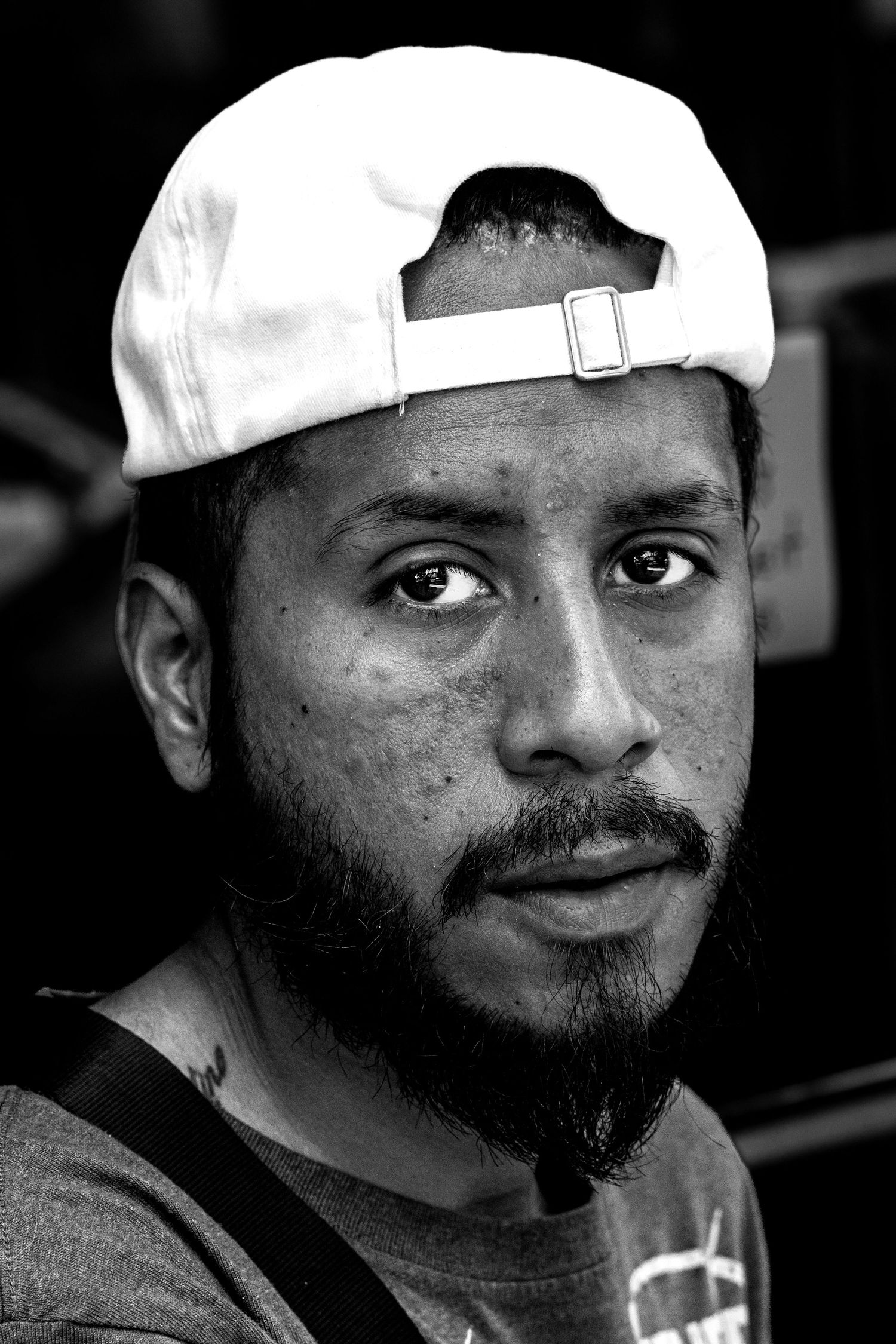Black and white portrait of a young man with a beard wearing a backwards white baseball cap.