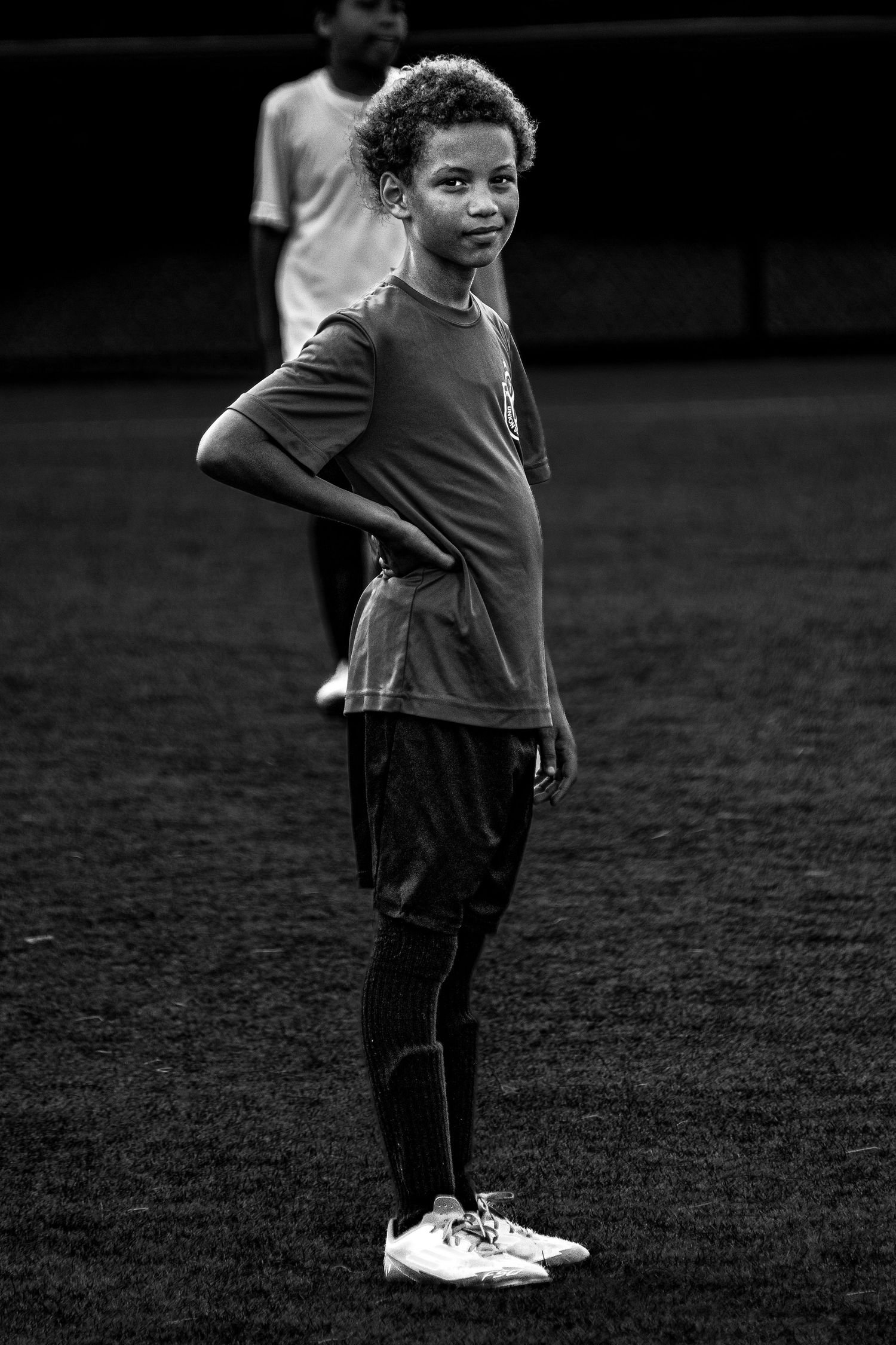 Young soccer player standing on field with hands on hips in black and white portrait.