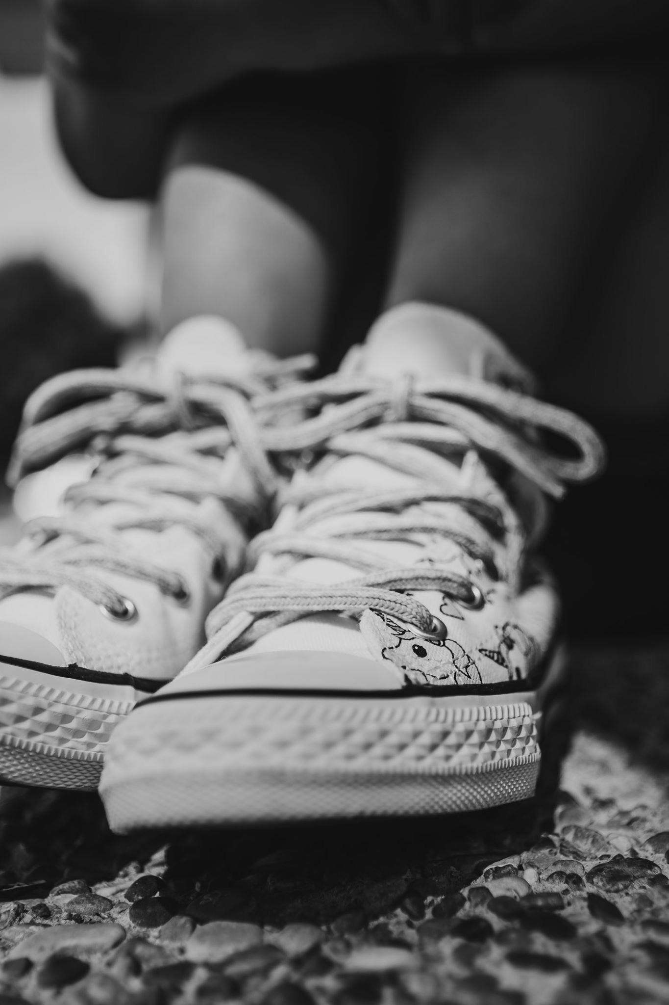Black and white close-up of Converse sneakers with cartoon print on childs feet.