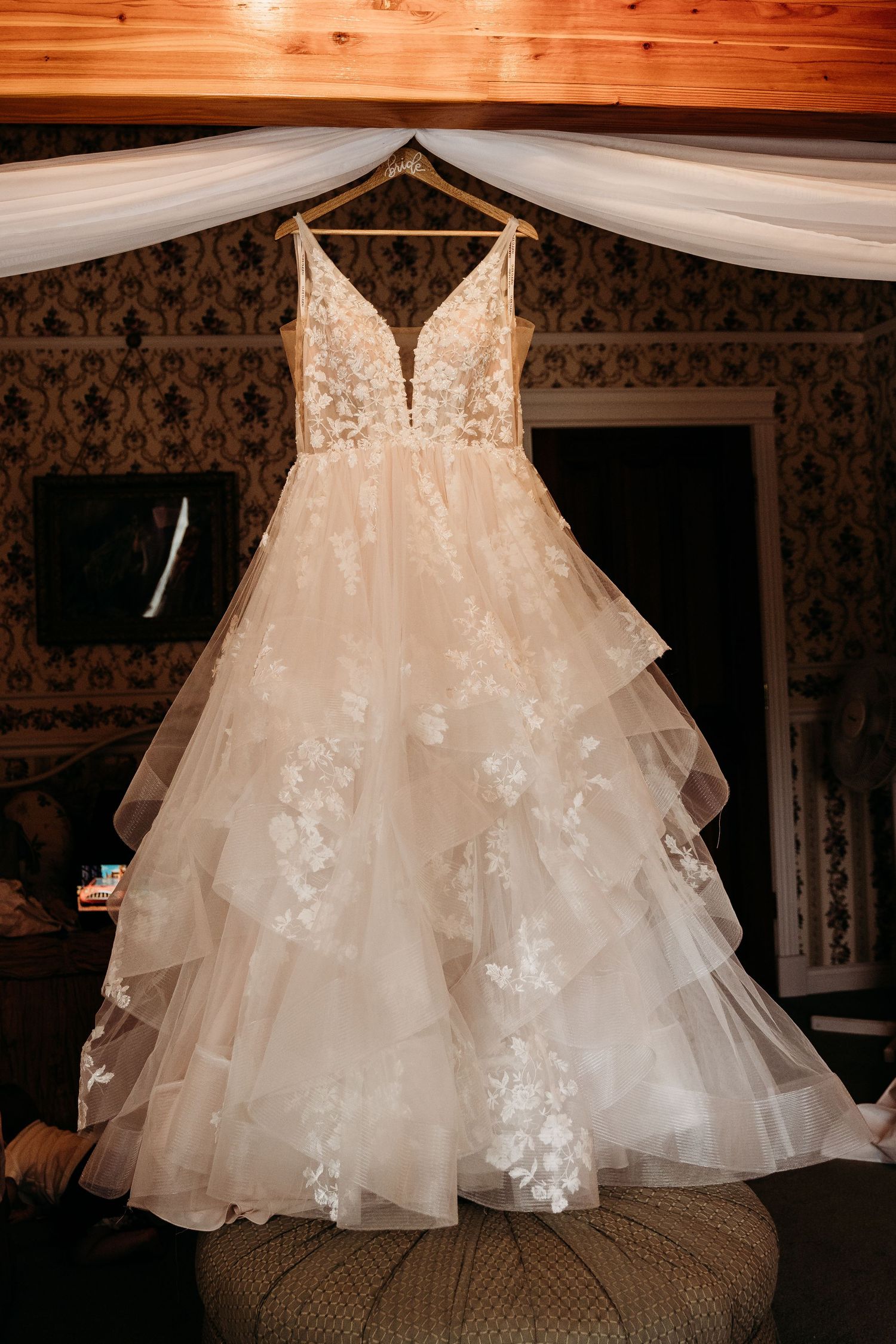 Elegant lace and tulle A-line wedding dress hanging in ornate vintage room.