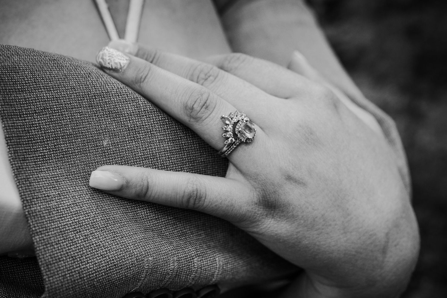 Close-up black and white photo of bride's hand showing a diamond halo engagement ring.