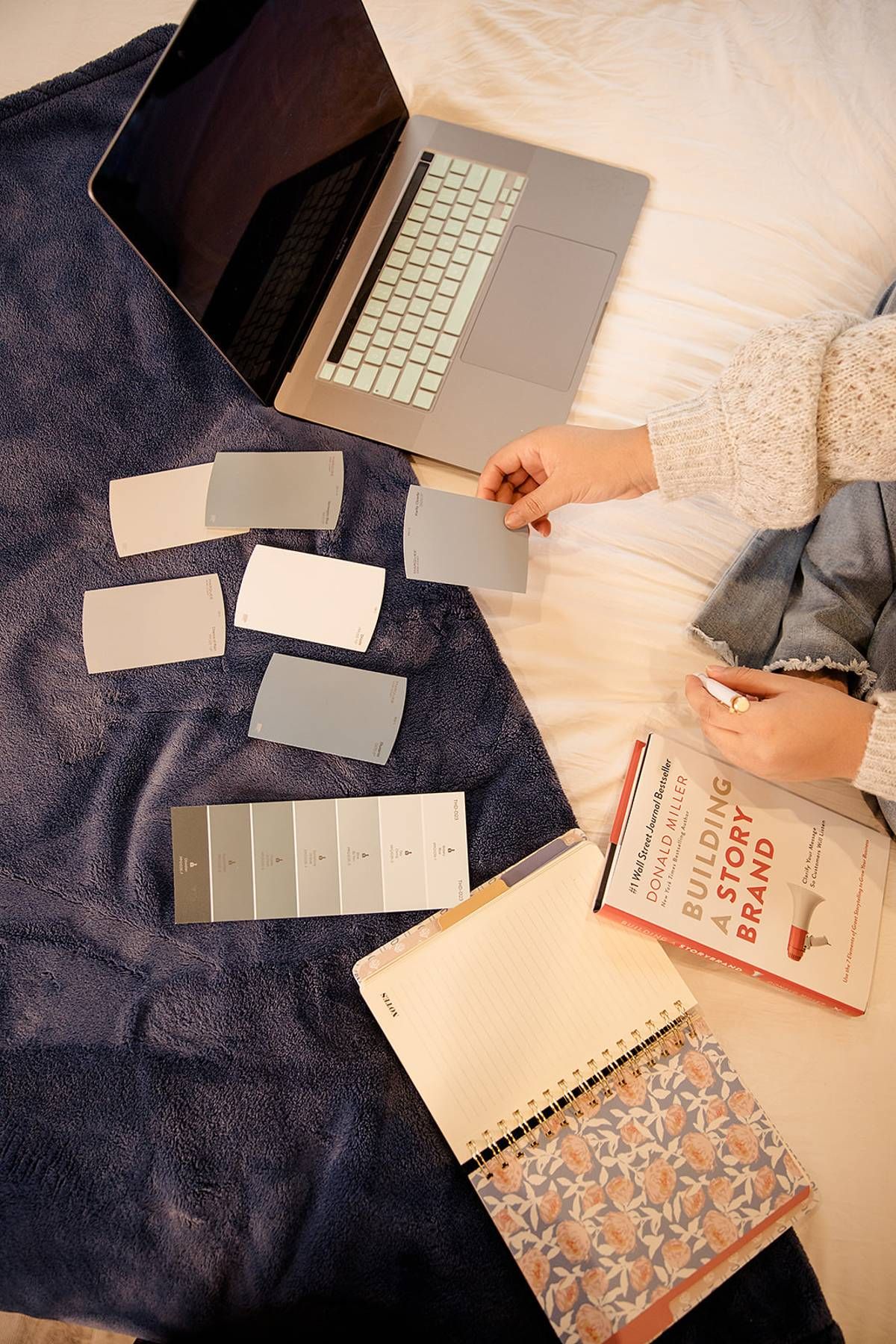 Overhead view of color swatches, laptop, and StoryBrand book on a navy blanket for brand design planning.
