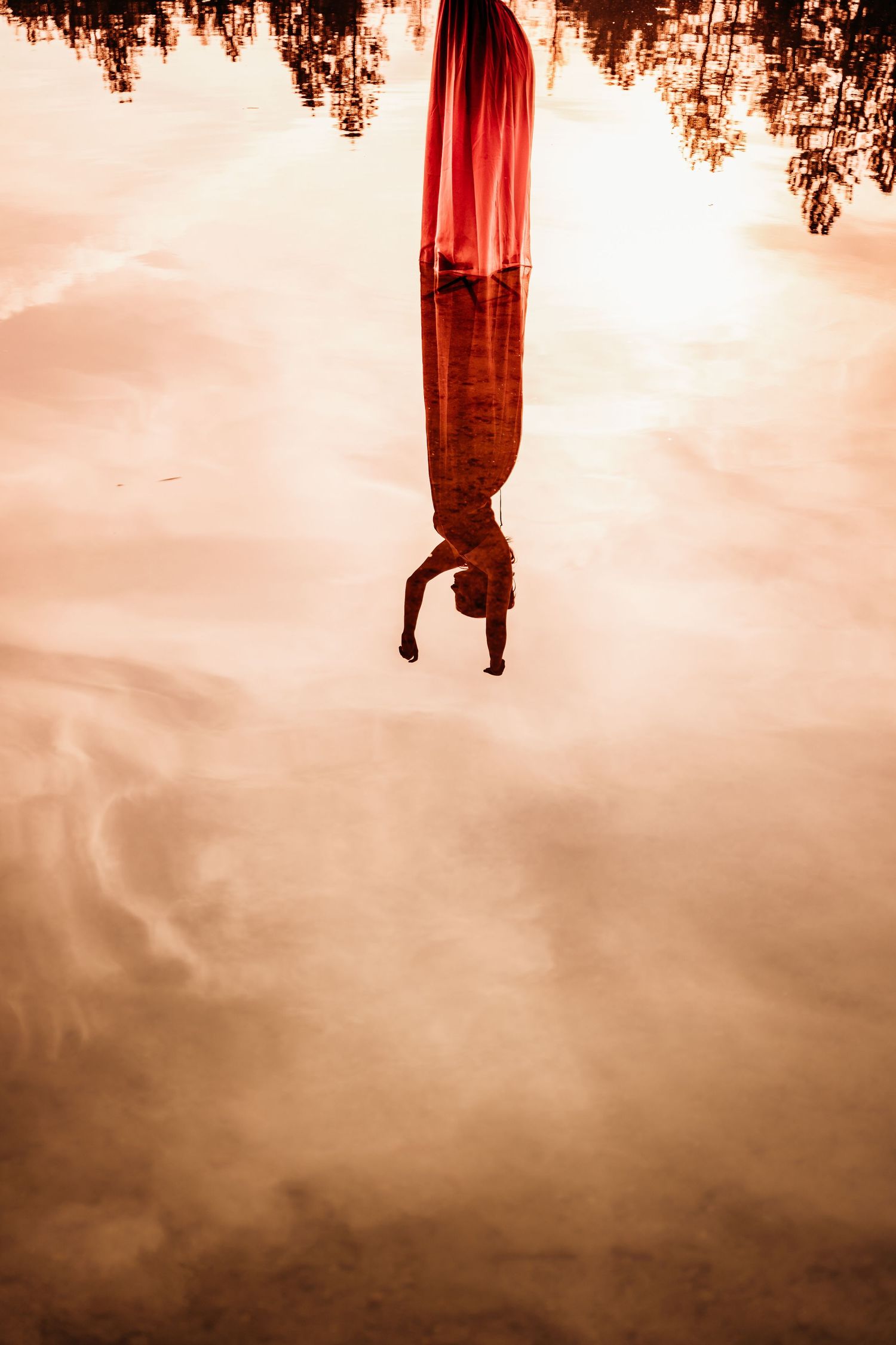 Surreal reflection of a person hanging upside down in still water with warm orange sunset tones.