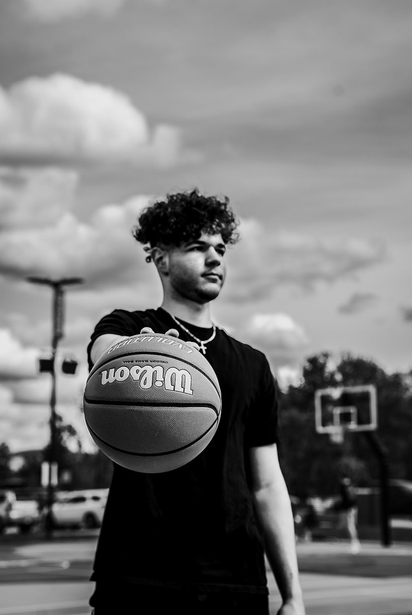 Young man holding a Wilson basketball on outdoor court in black and white photo.
