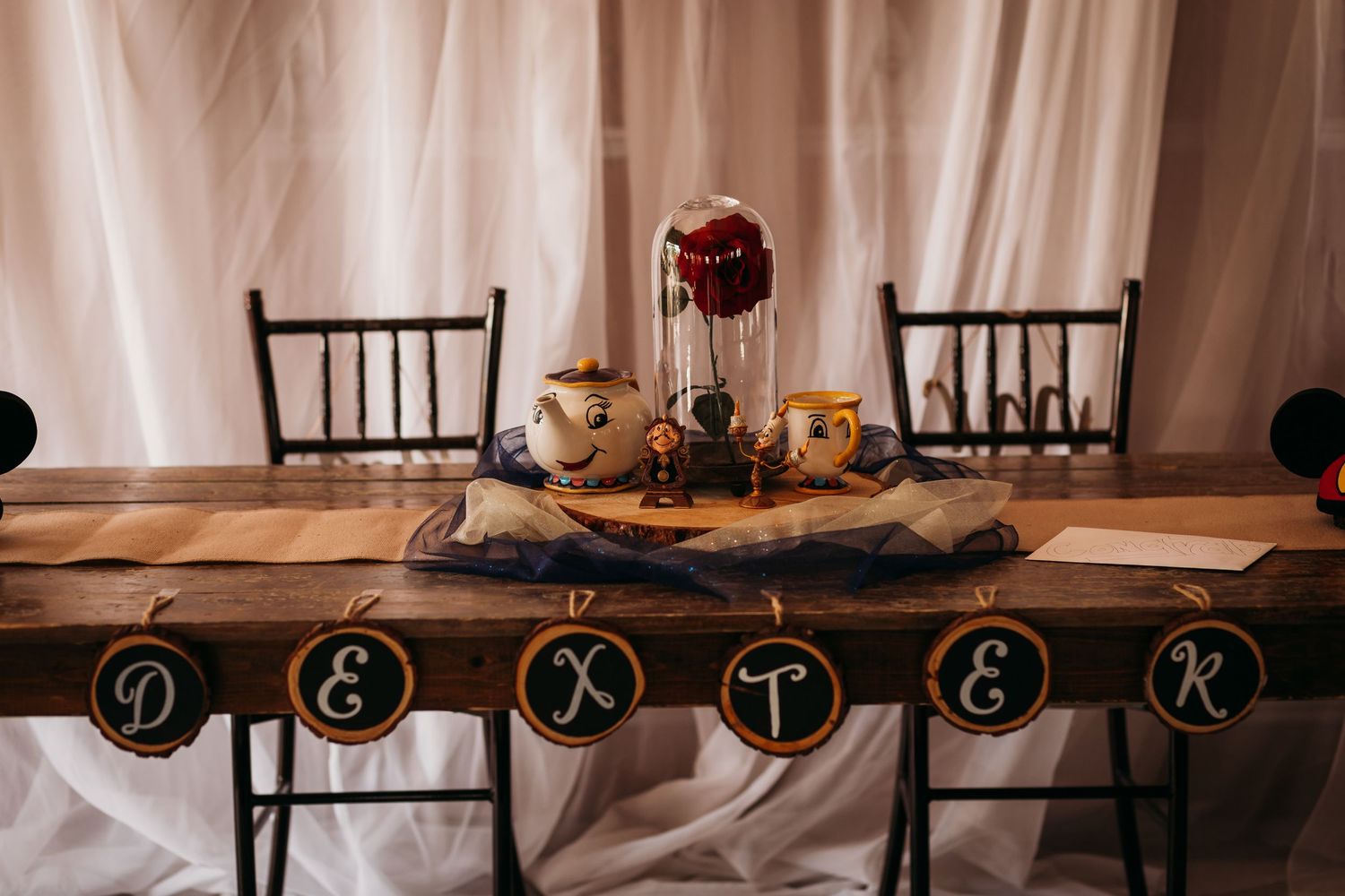 Beauty and the Beast themed wedding head table with enchanted rose centerpiece and character figurines.