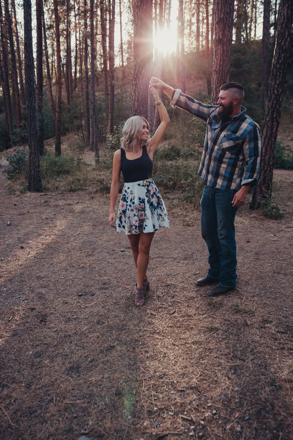 Couple dancing in pine forest with sunlight streaming through trees.