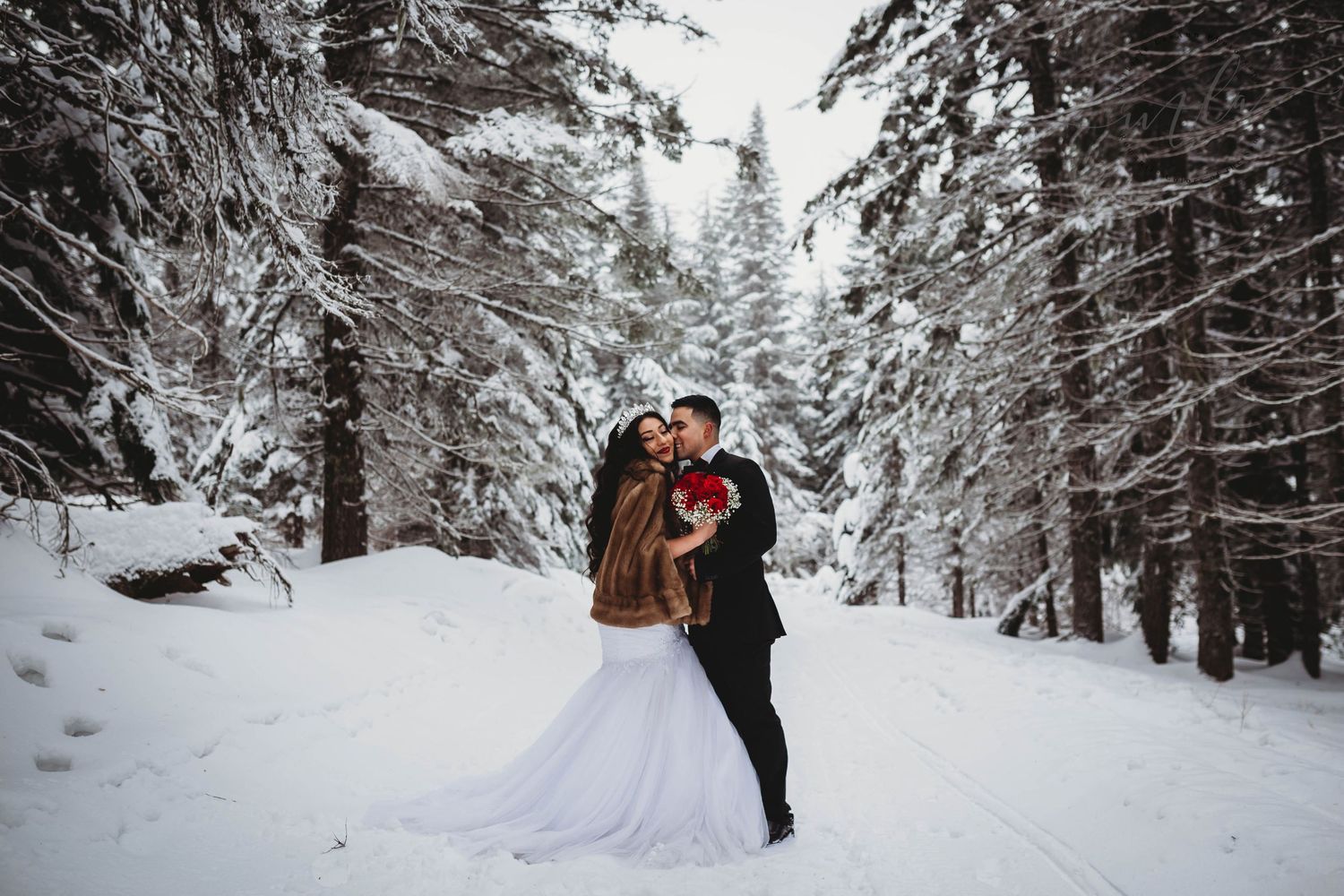 Couple shares romantic kiss in stunning snowy winter forest wedding portrait.