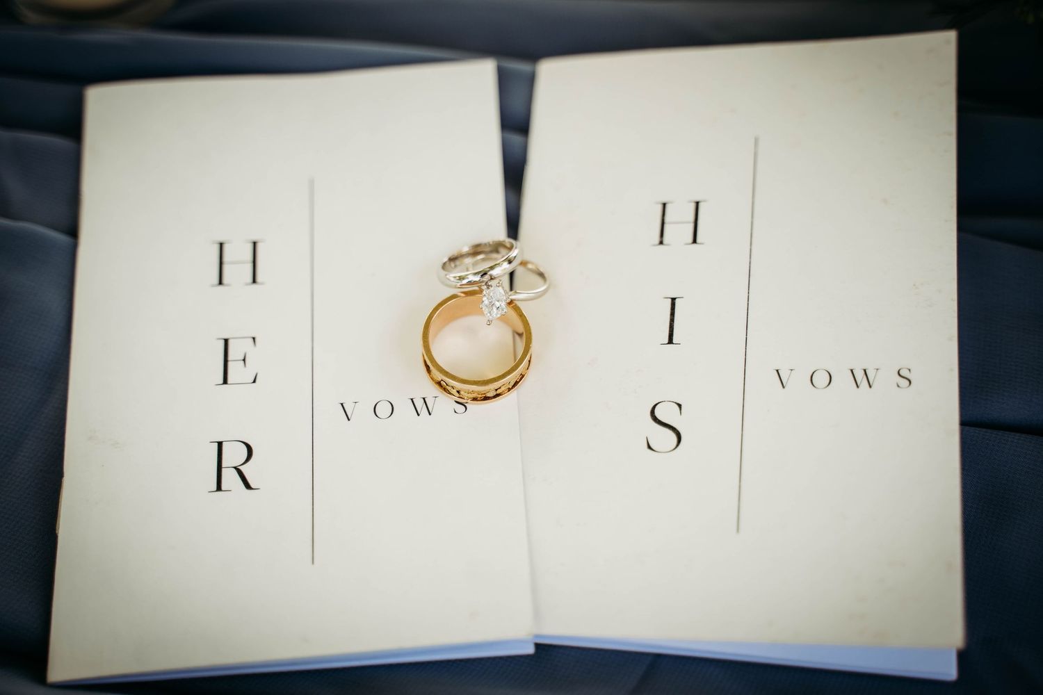 His and her wedding vow booklets lay open with gold engagement and wedding rings placed on top.