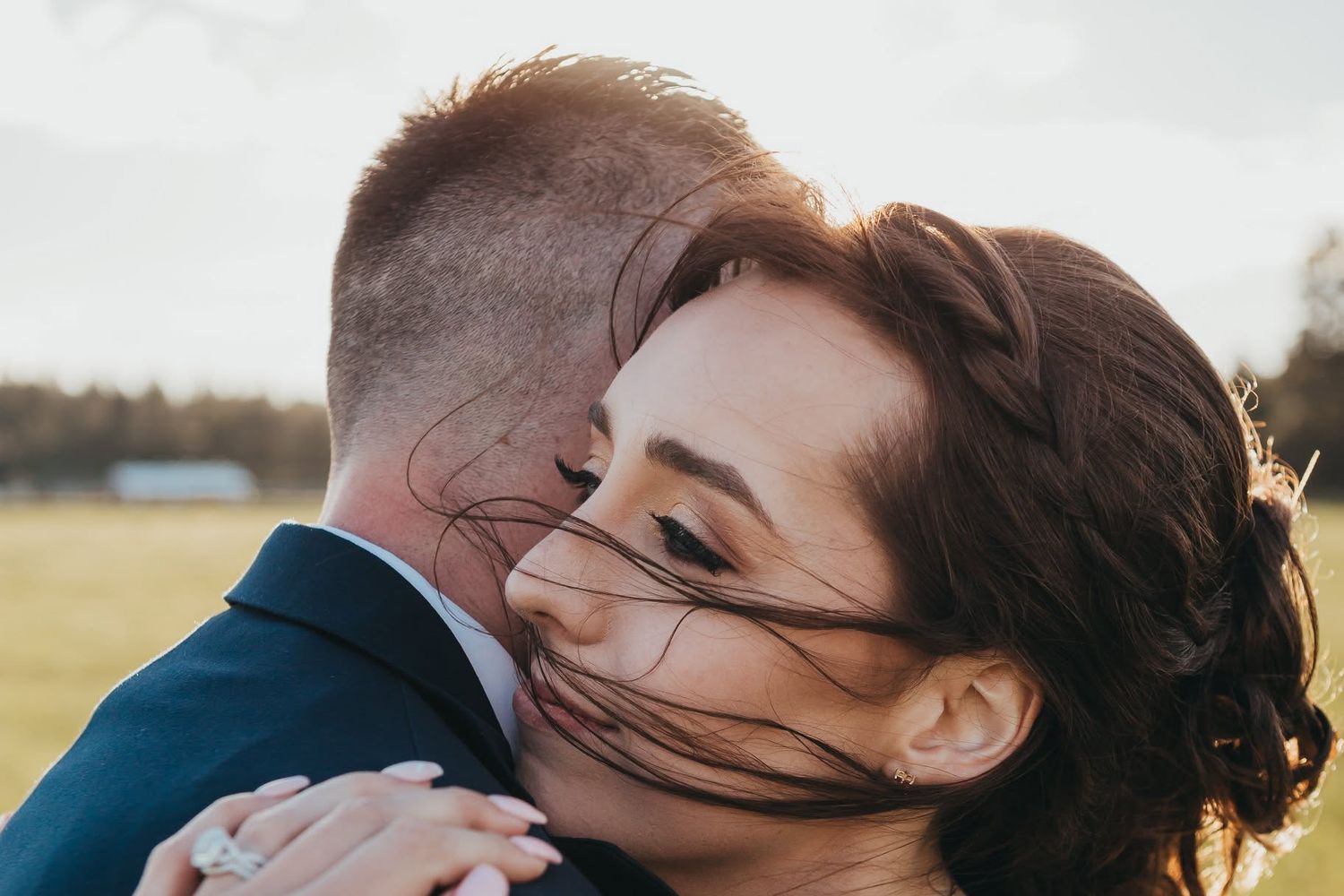 Bride embracing groom in a tender moment at golden hour outdoor wedding celebration.
