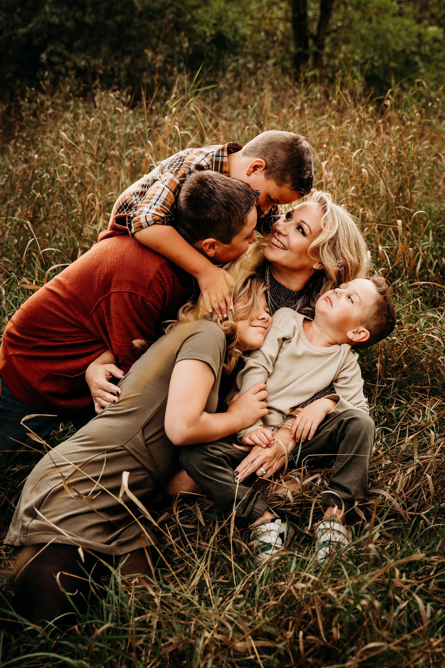 Mother surrounded by three children hugging and laughing in tall autumn grass.