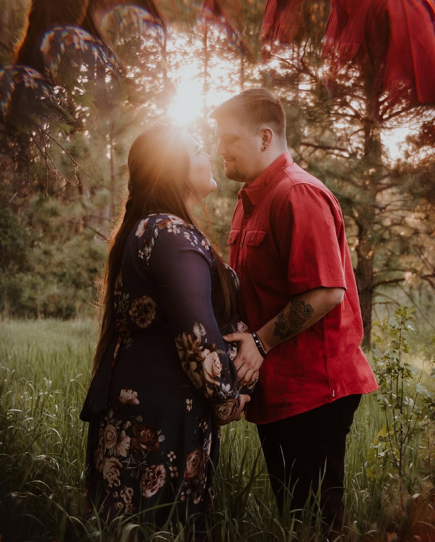 Couple holding hands facing each other in forest at golden sunset.