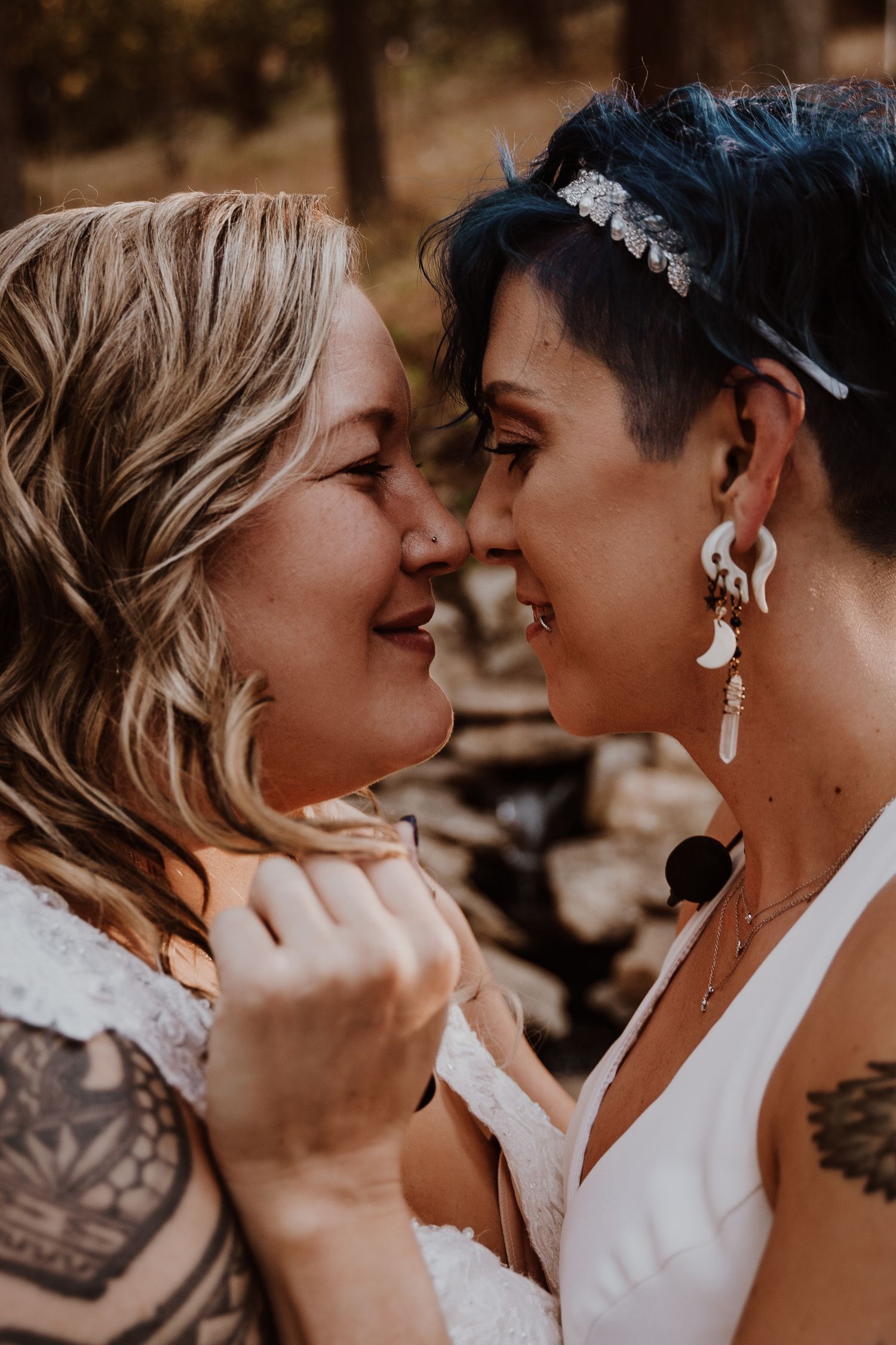 Close-up of two brides with tattoos smiling and touching foreheads in an outdoor wedding.