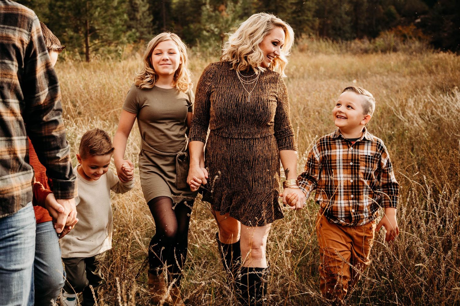 Family walking hand in hand through golden autumn meadow grass in fall outfits.