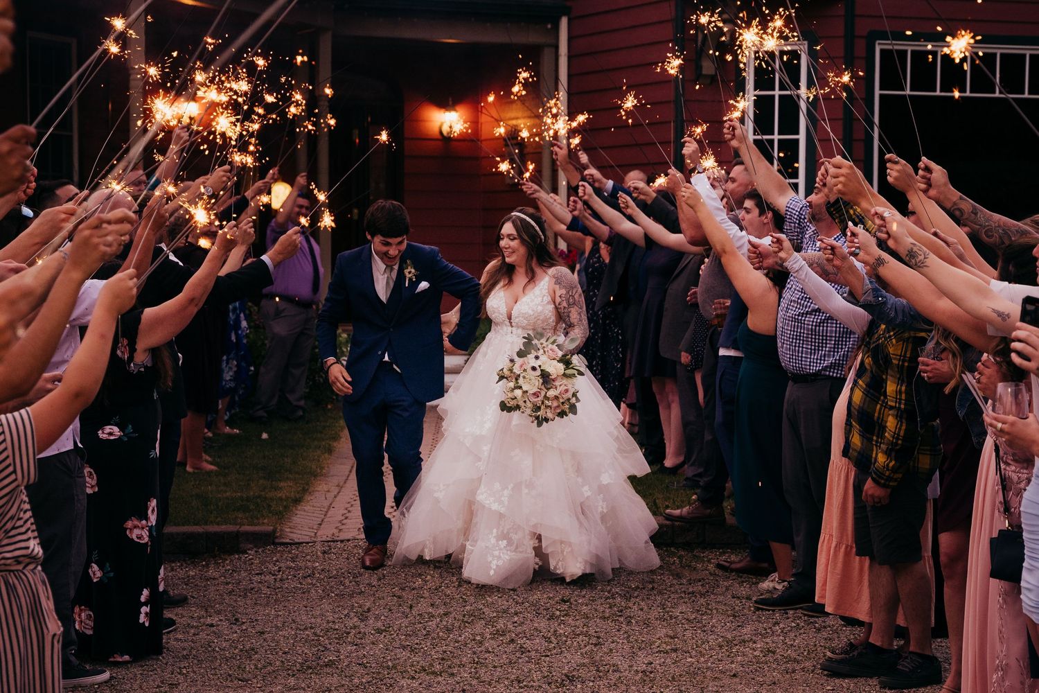 Bride and groom walk through sparkler tunnel surrounded by cheering guests during wedding send-off.