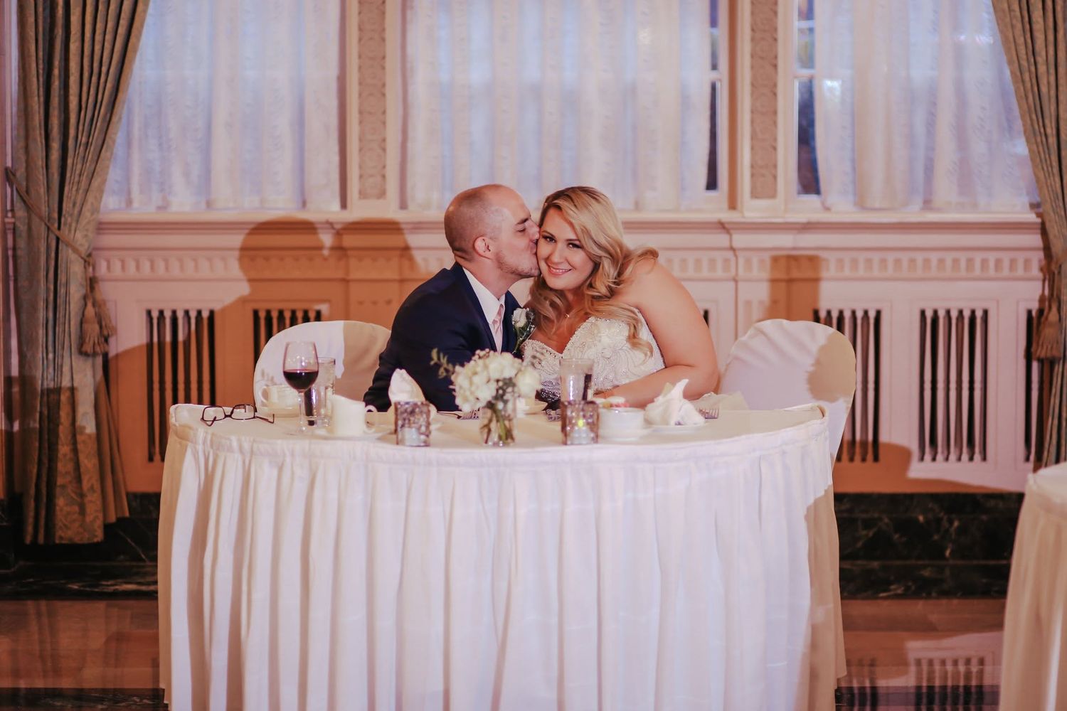 Bride and groom share a kiss at sweetheart table during wedding reception.