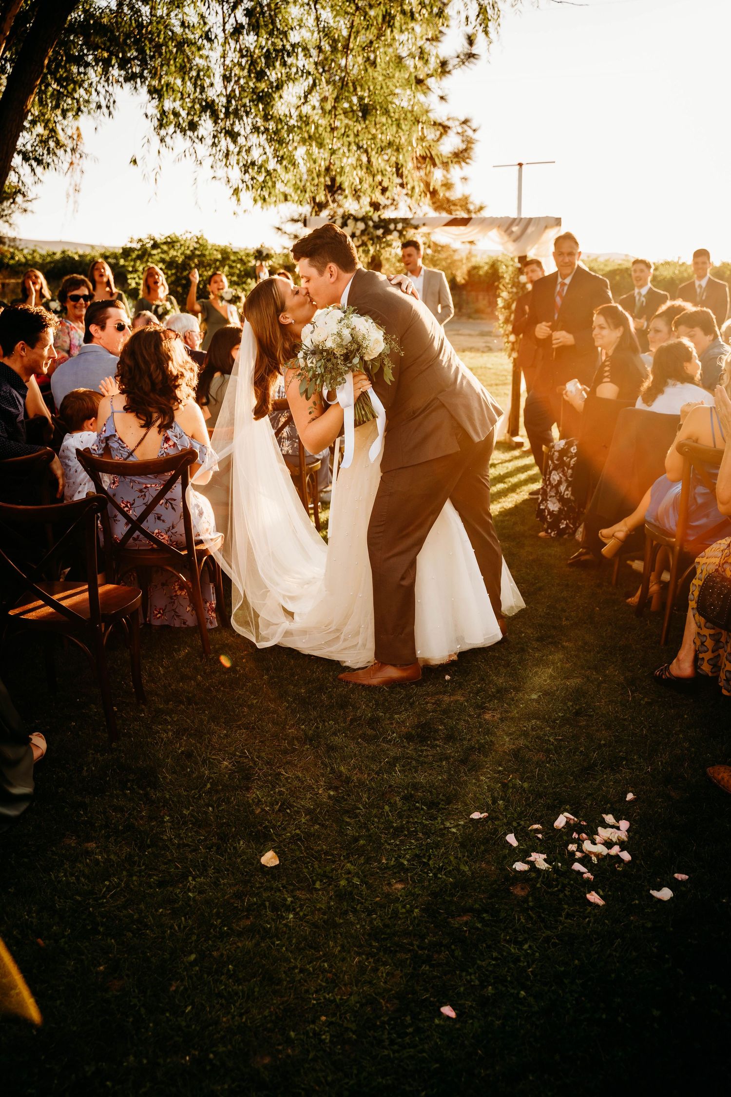 Bride and groom share a first kiss as newlyweds while walking the aisle at golden hour outdoor ceremony.