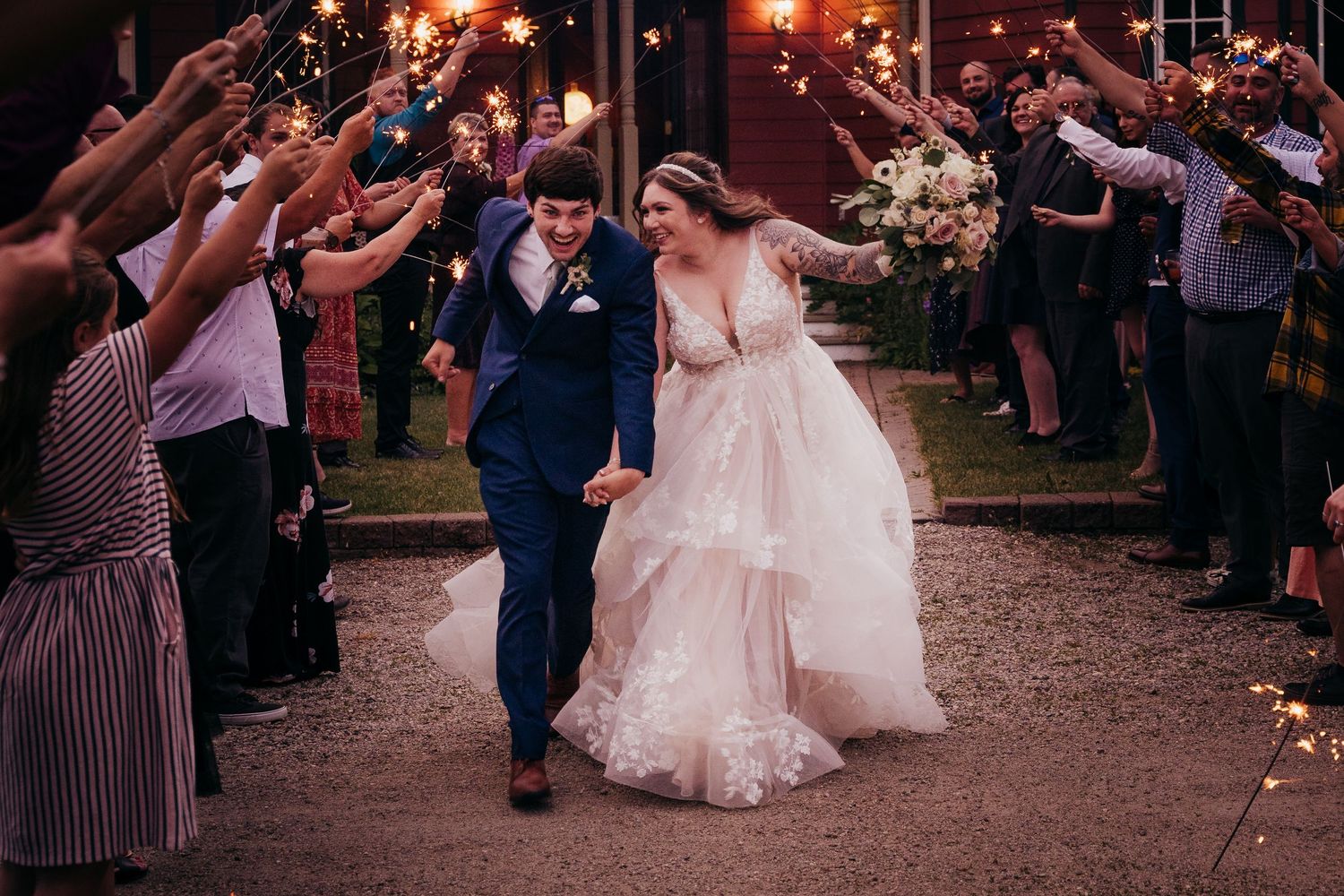 Bride and groom walk hand-in-hand through a glowing sparkler tunnel at their wedding reception.