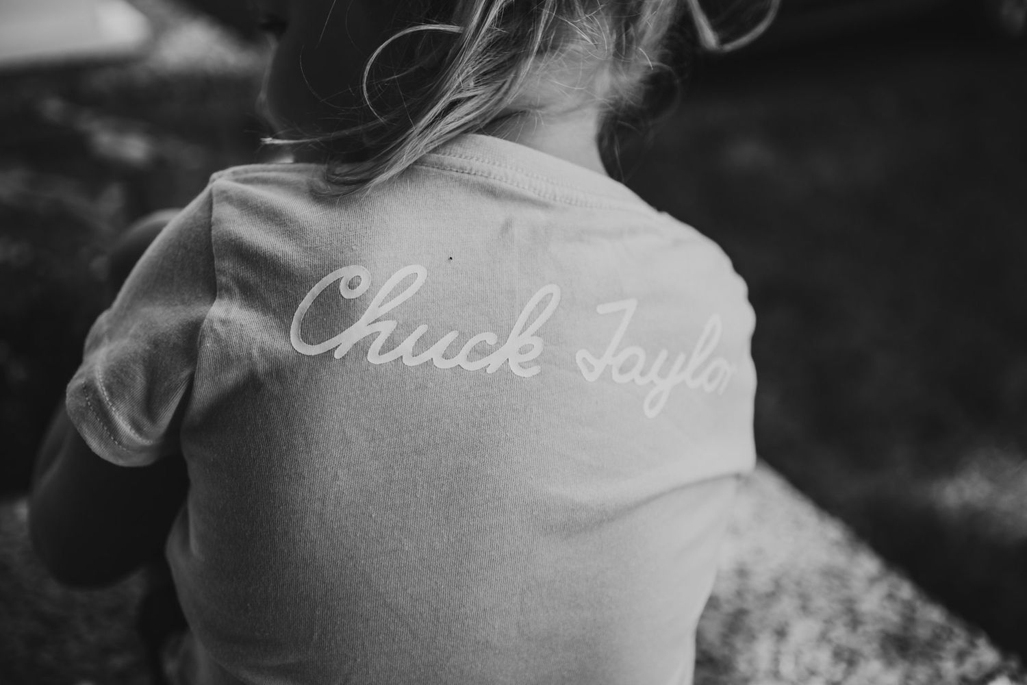 Close-up black and white photo of child wearing Chuck Taylor Converse t-shirt from behind.
