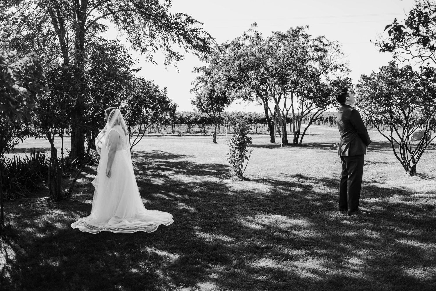 Black and white photo of bride in flowing veil and groom sharing a first look moment outdoors.