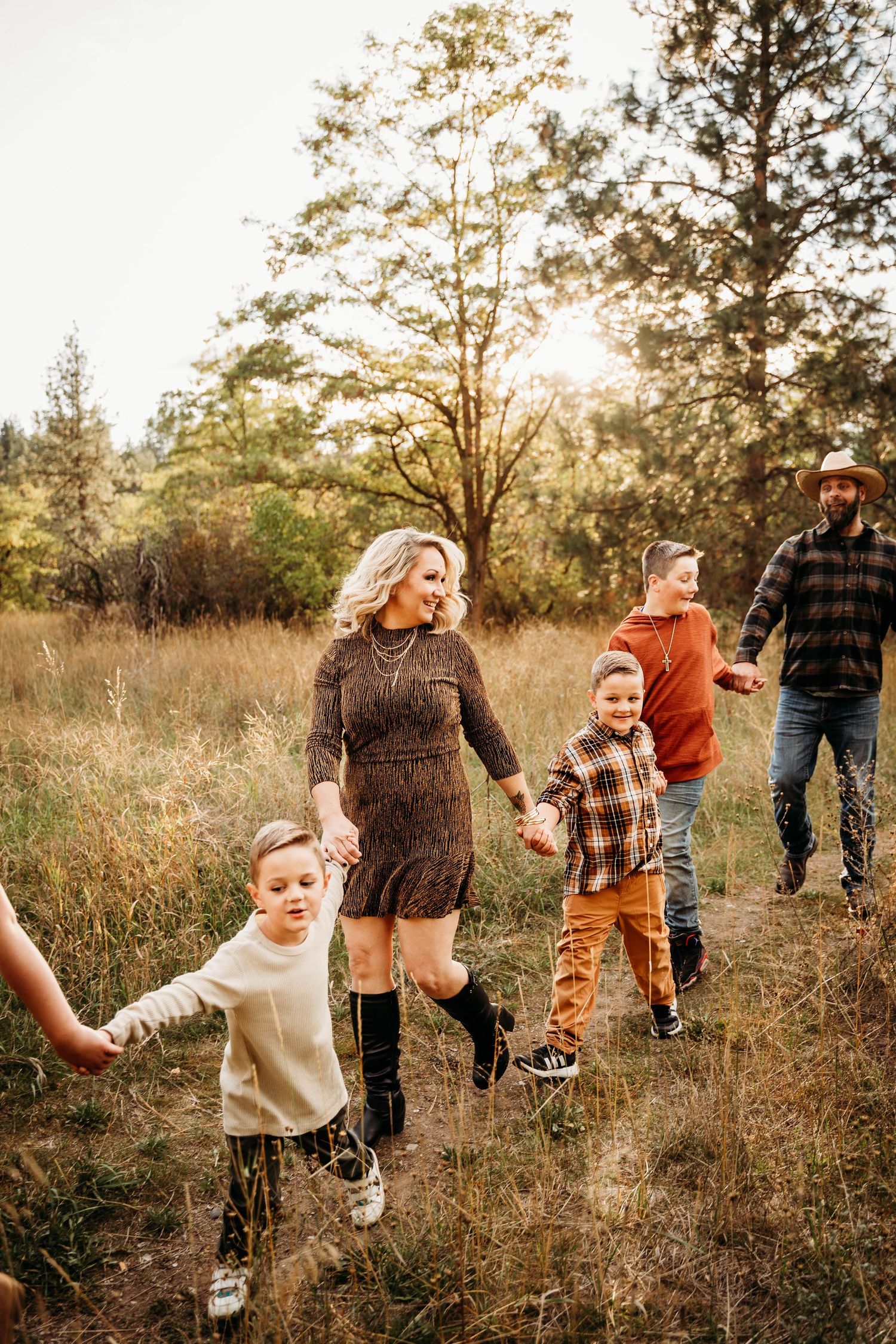 Family walking through a sunlit autumn field at golden hour in casual fall attire.
