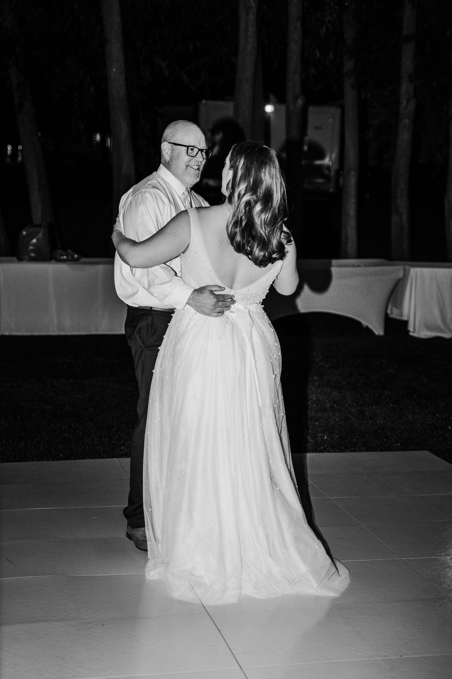 Black and white photo of bride sharing an emotional father-daughter dance at night.