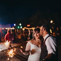 Bride and groom holding sparklers at night during outdoor wedding reception celebration.