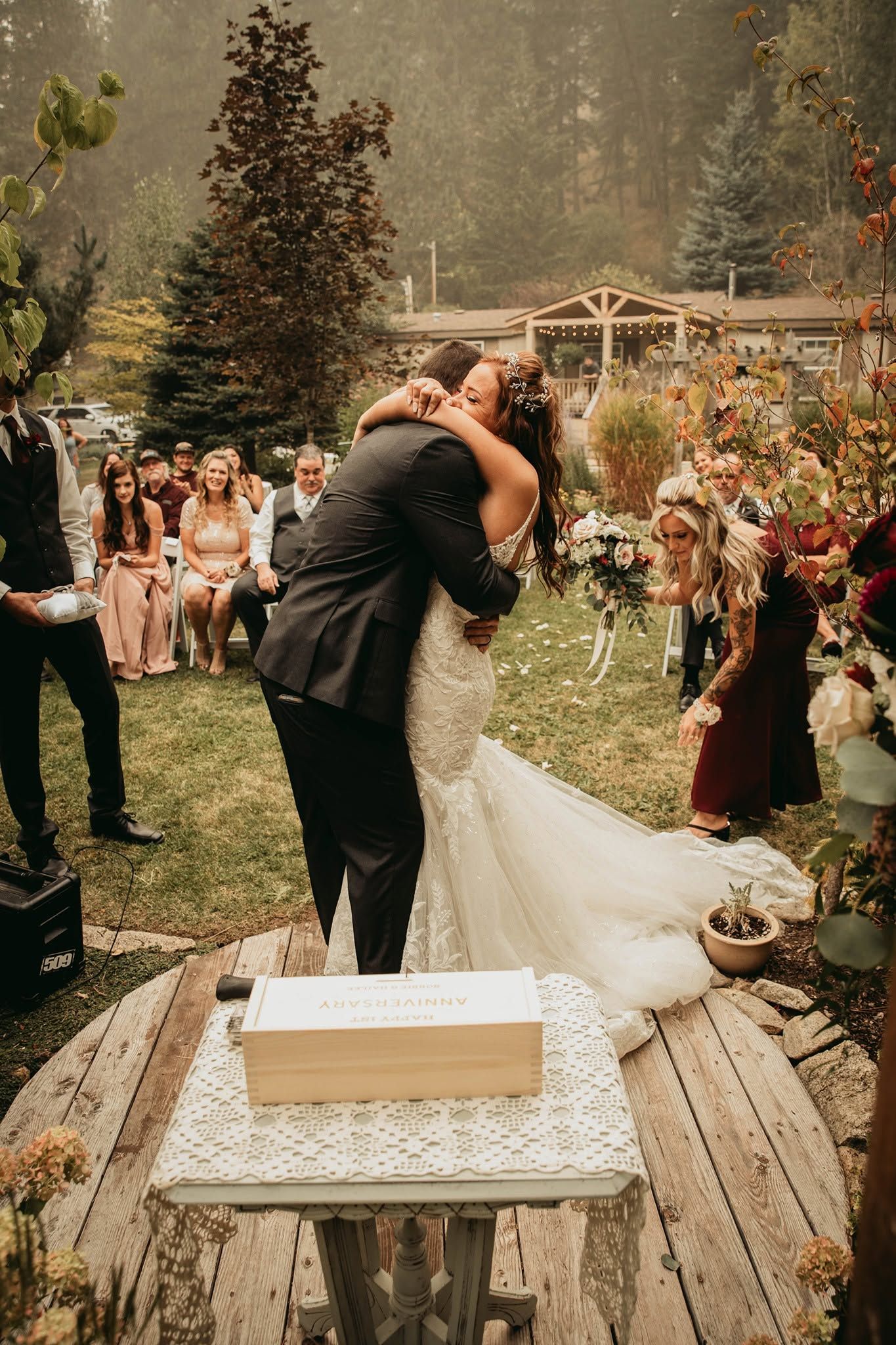 Bride and groom sharing first kiss at outdoor wedding ceremony surrounded by guests.
