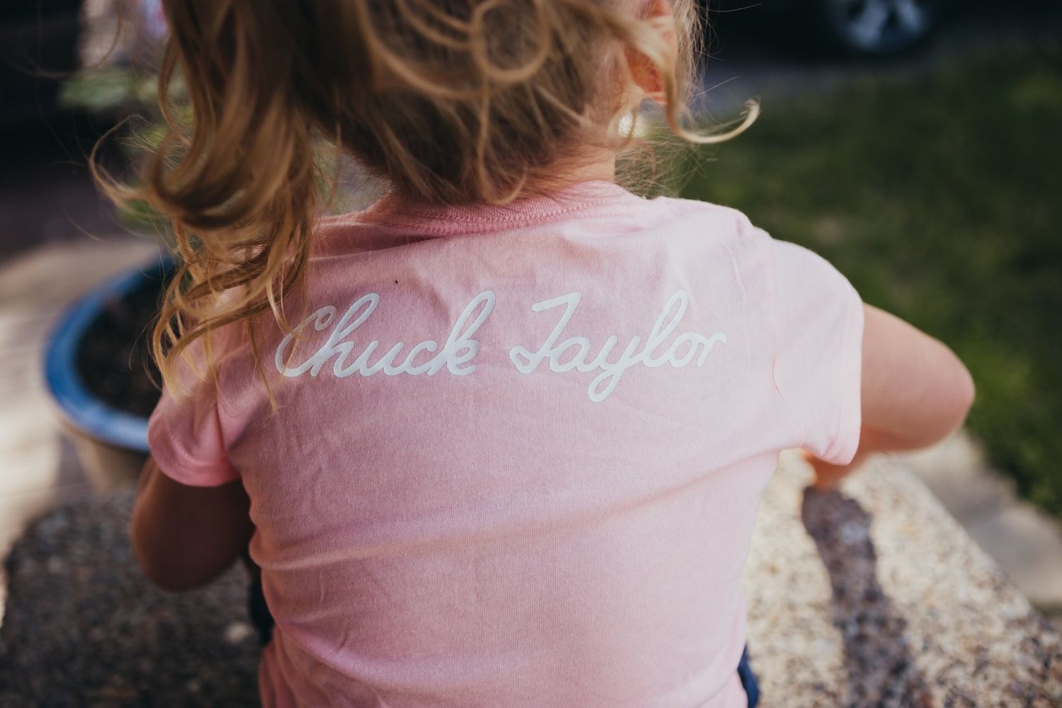 Back view of a young girl wearing a pink Converse Chuck Taylor t-shirt outdoors.