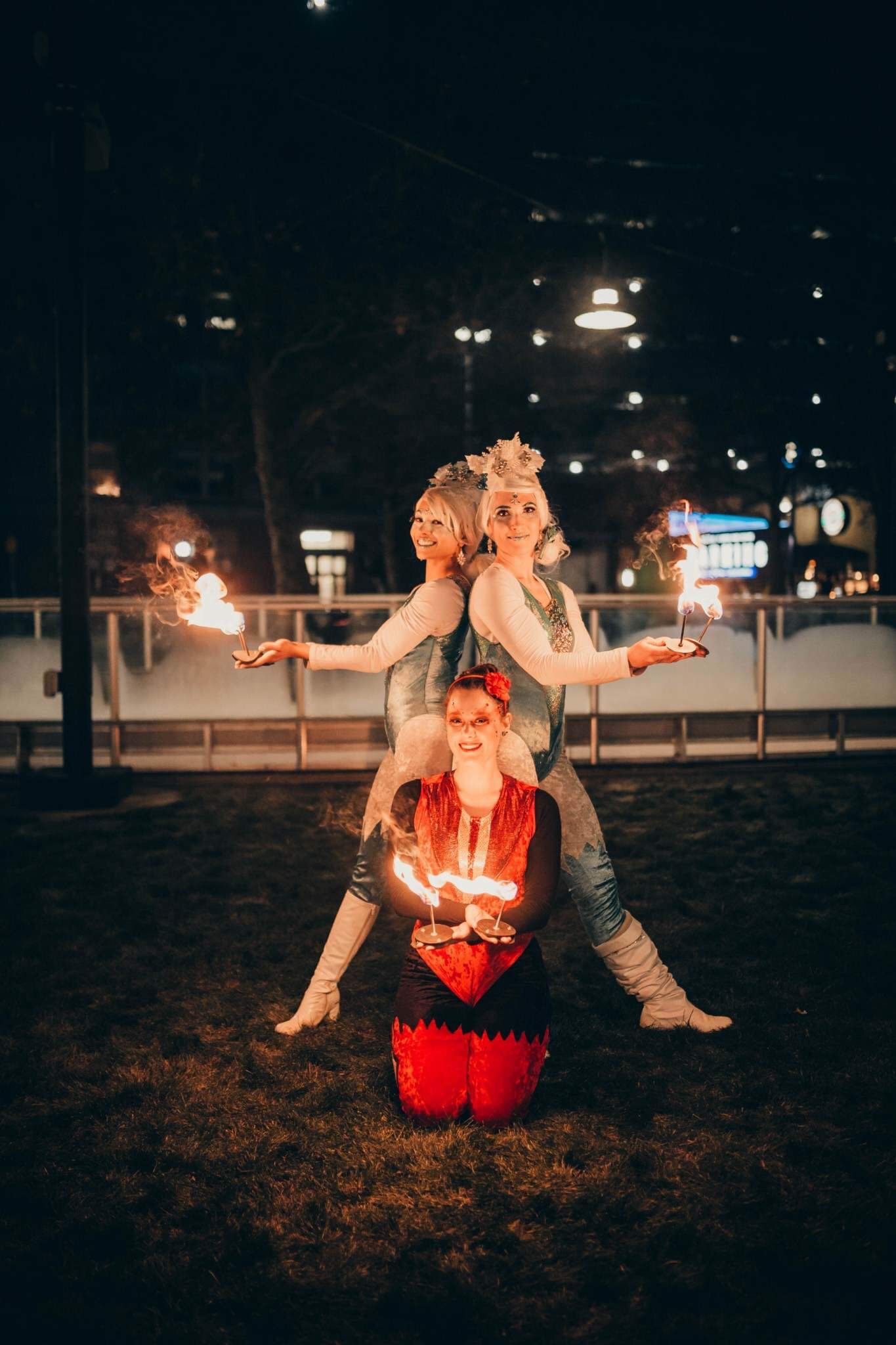 Three costumed fire performers posing with flames at night during outdoor entertainment show.
