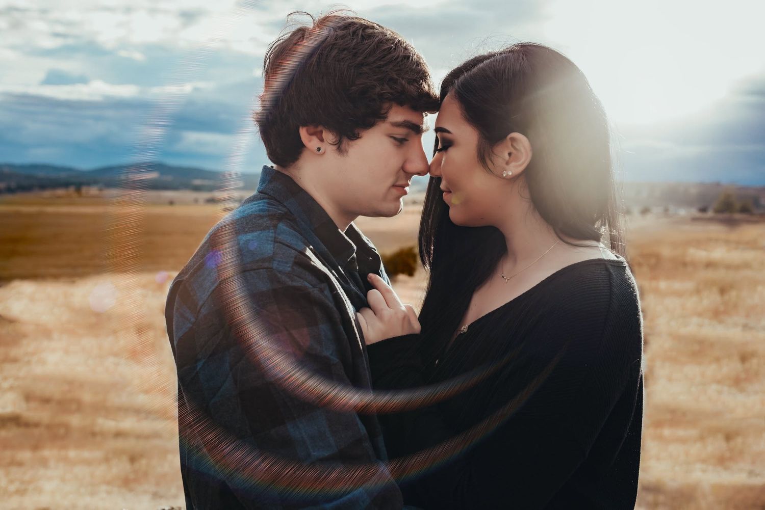 Romantic couple almost kissing in golden field under dramatic sky.