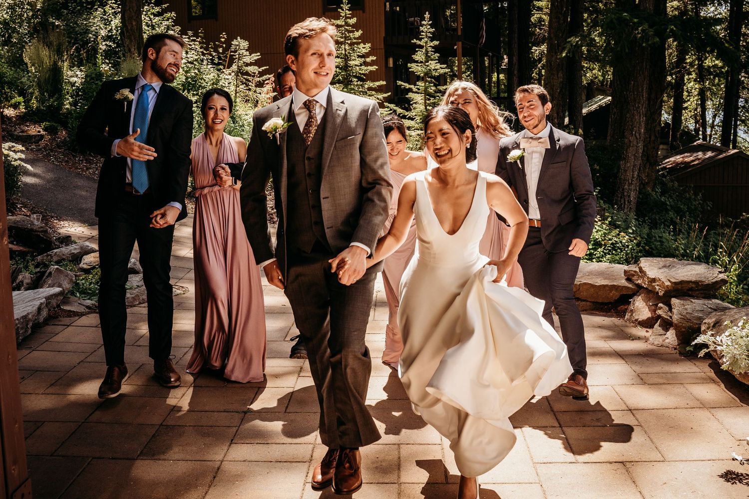Bride and groom walking joyfully with wedding party on a sunlit outdoor venue patio.