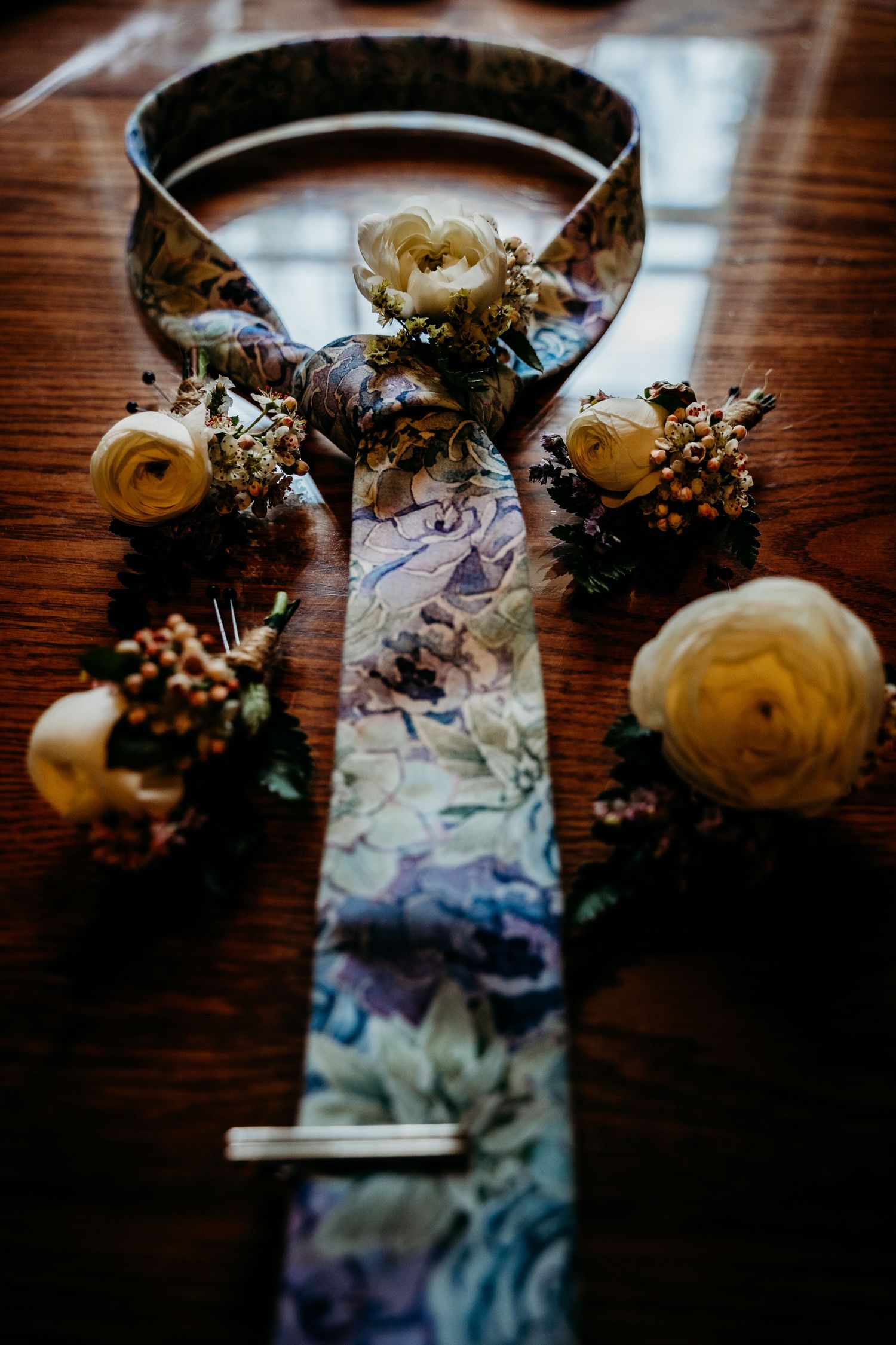 Floral patterned wedding tie and boutonniere flowers arranged artfully on a wooden surface.